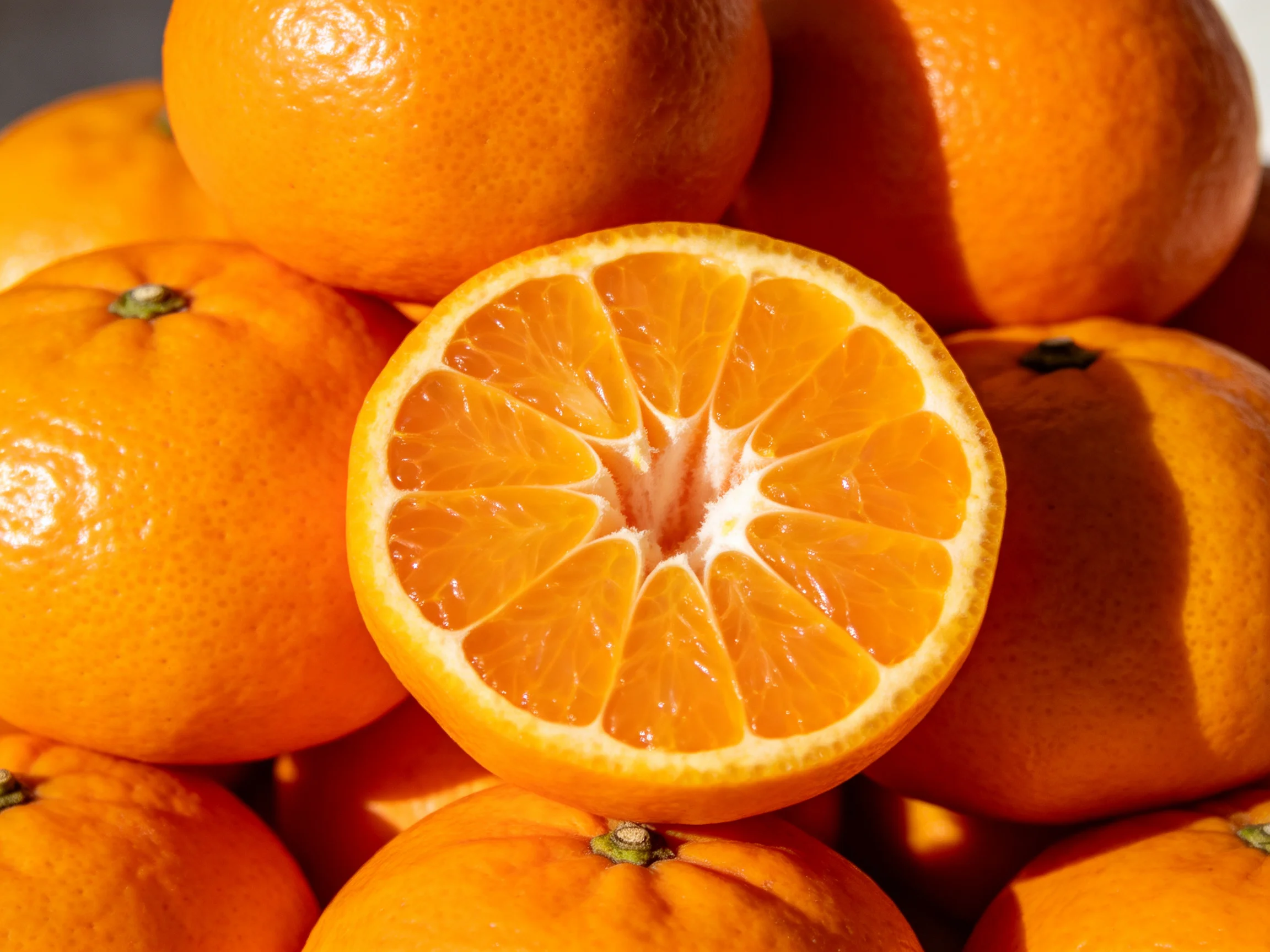 A pile of vibrant oranges with one halved orange displayed prominently