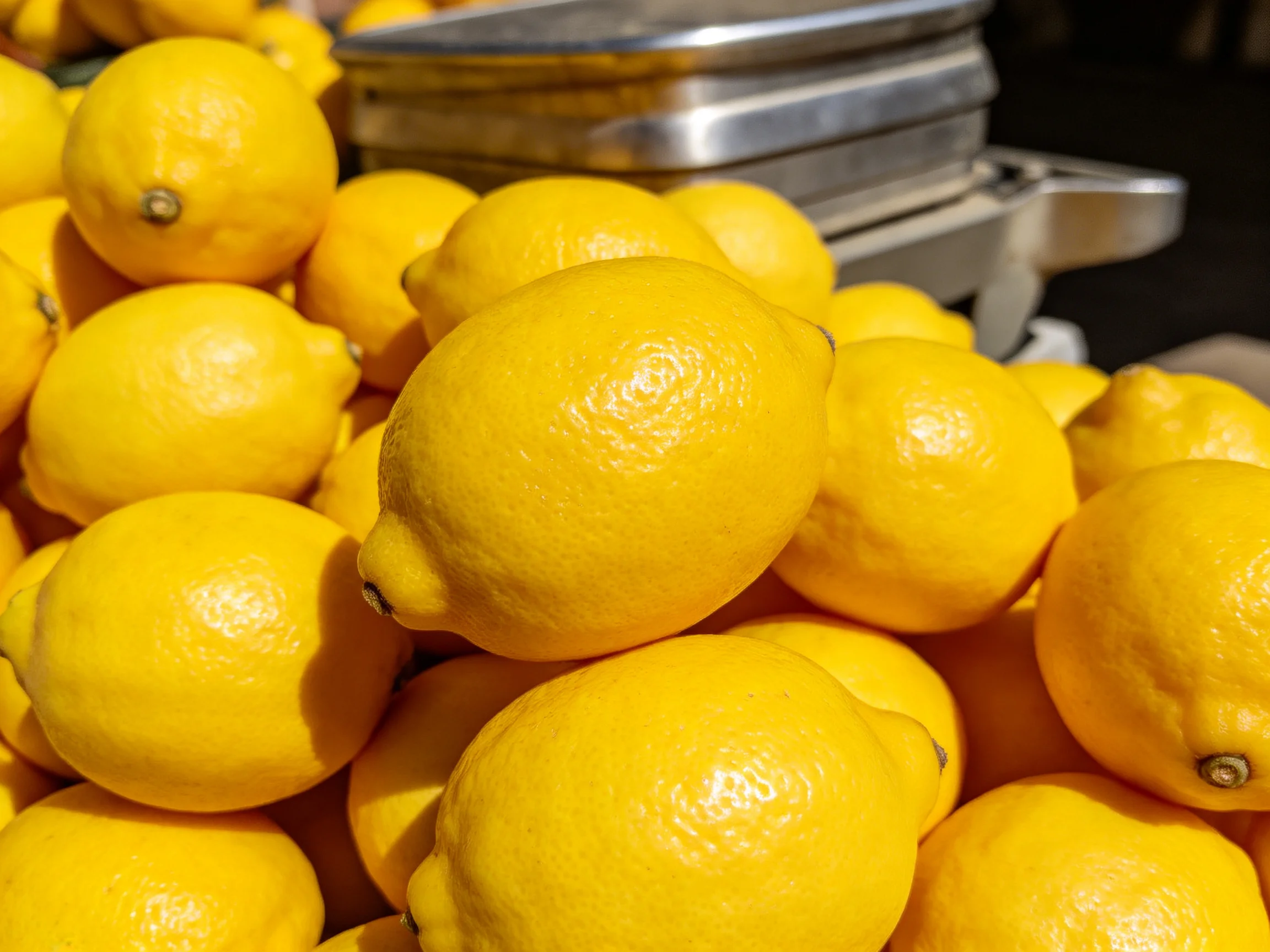 A pile of vibrant yellow lemons stacked near metallic containers