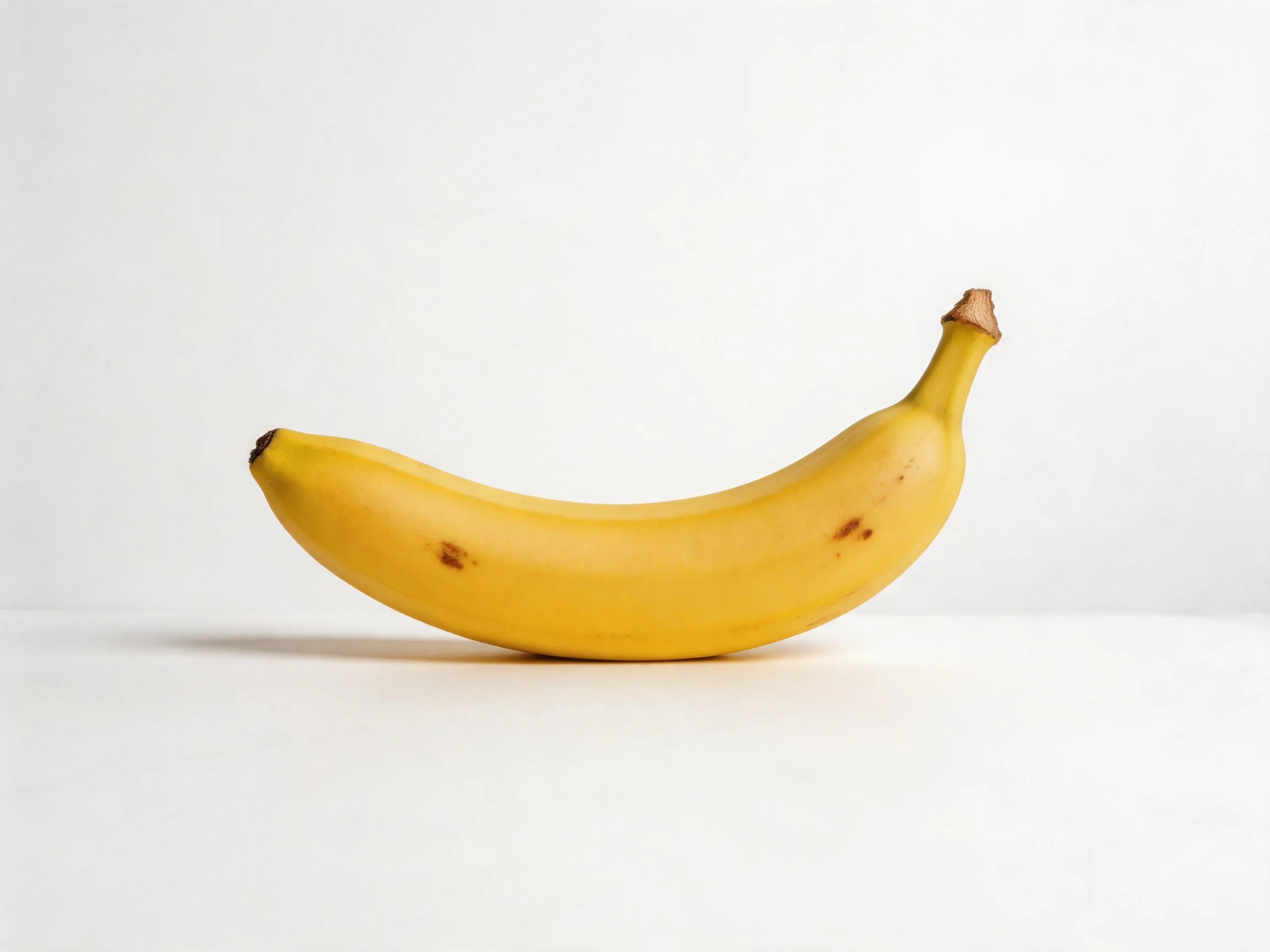 A ripe yellow banana with brown spots on a plain white surface