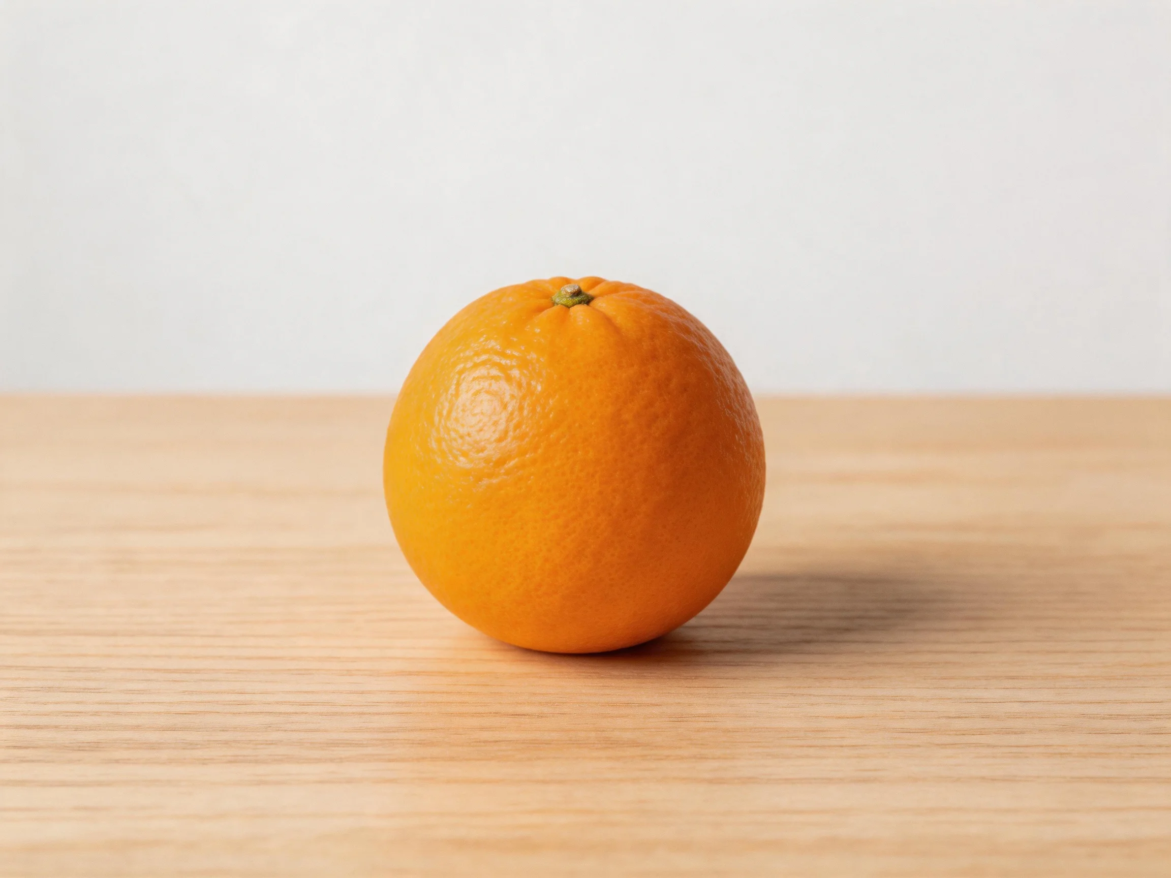 A single bright orange rests on a light wooden surface