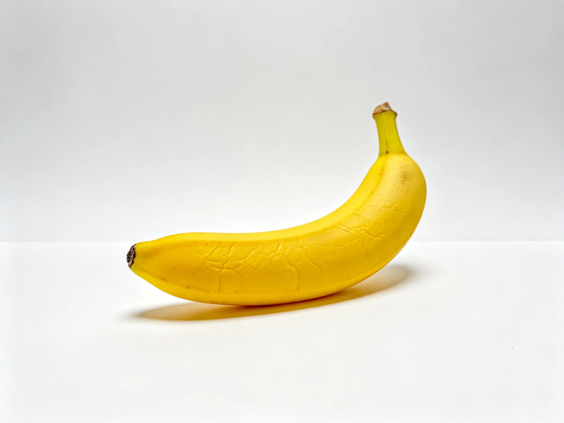 A single bright yellow banana positioned on a stark white surface