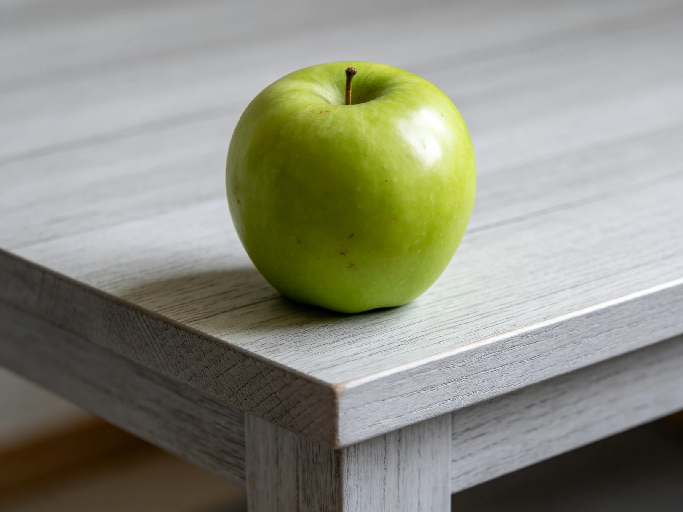 A single glossy green apple rests on a light gray wooden table