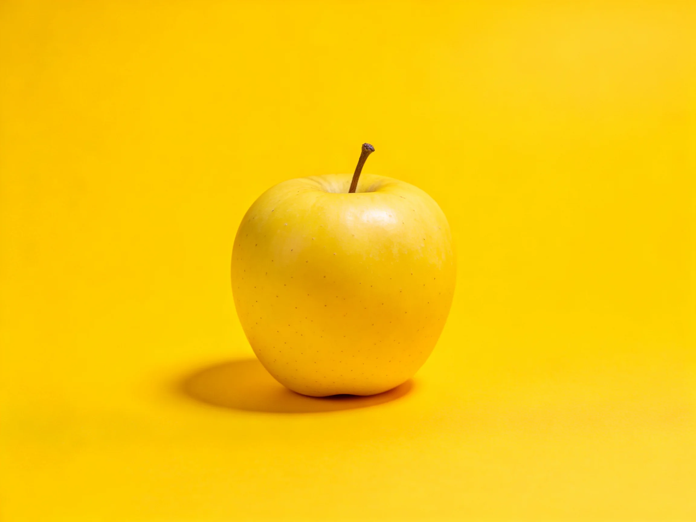 A single golden-yellow apple centered on a solid yellow backdrop