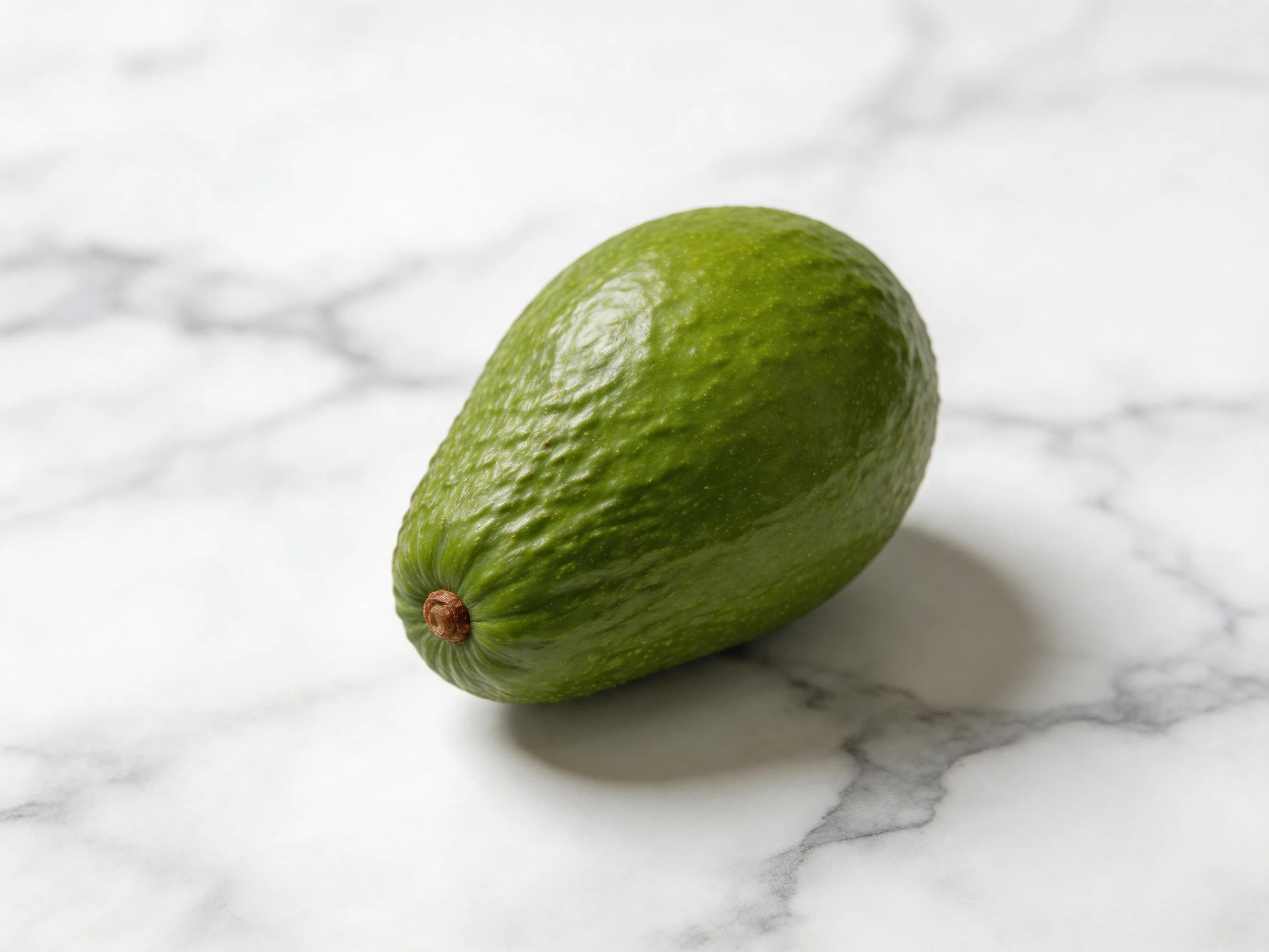 A single green avocado rests on a white marble surface