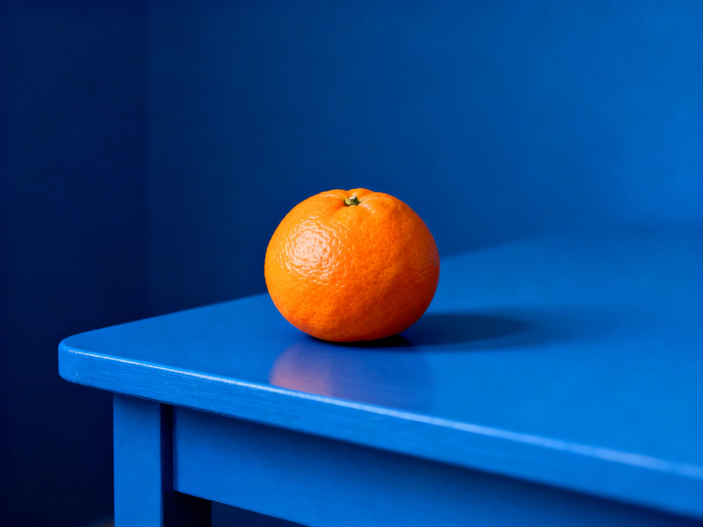 A single orange sits on a vibrant blue table with a matching blue backdrop