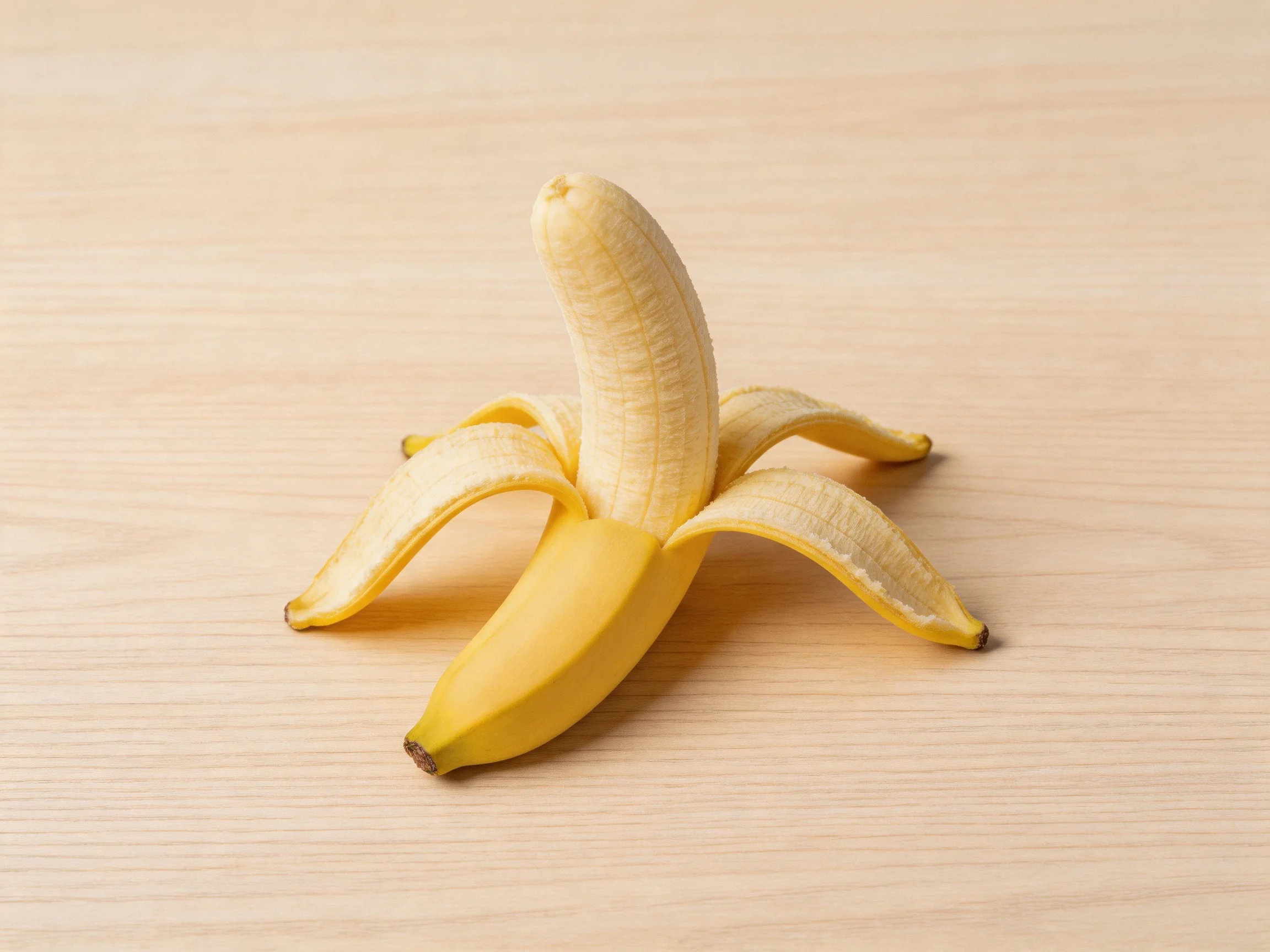 A single peeled yellow banana rests on a light wooden surface