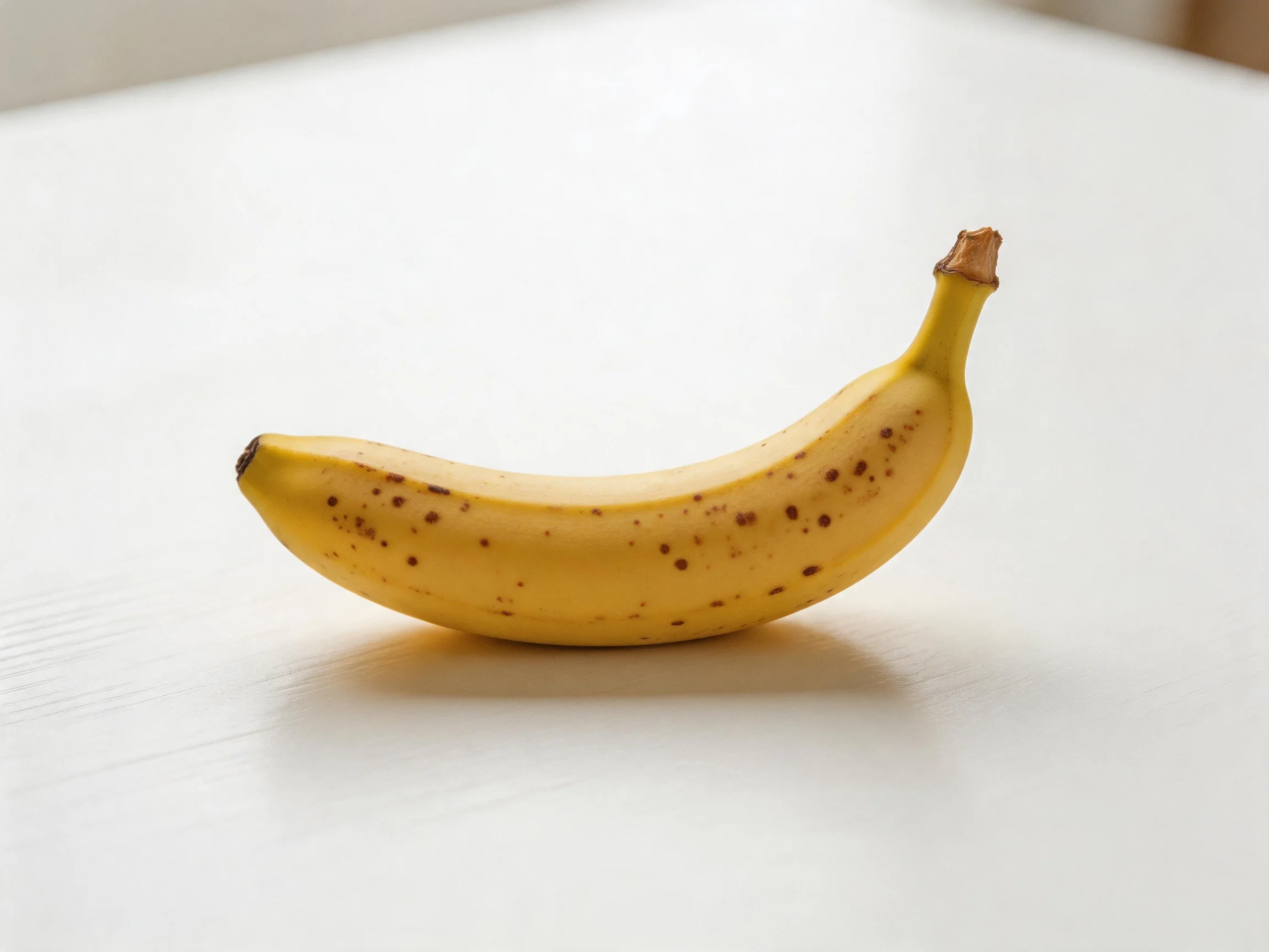 A single ripe banana with brown spots rests on a white surface