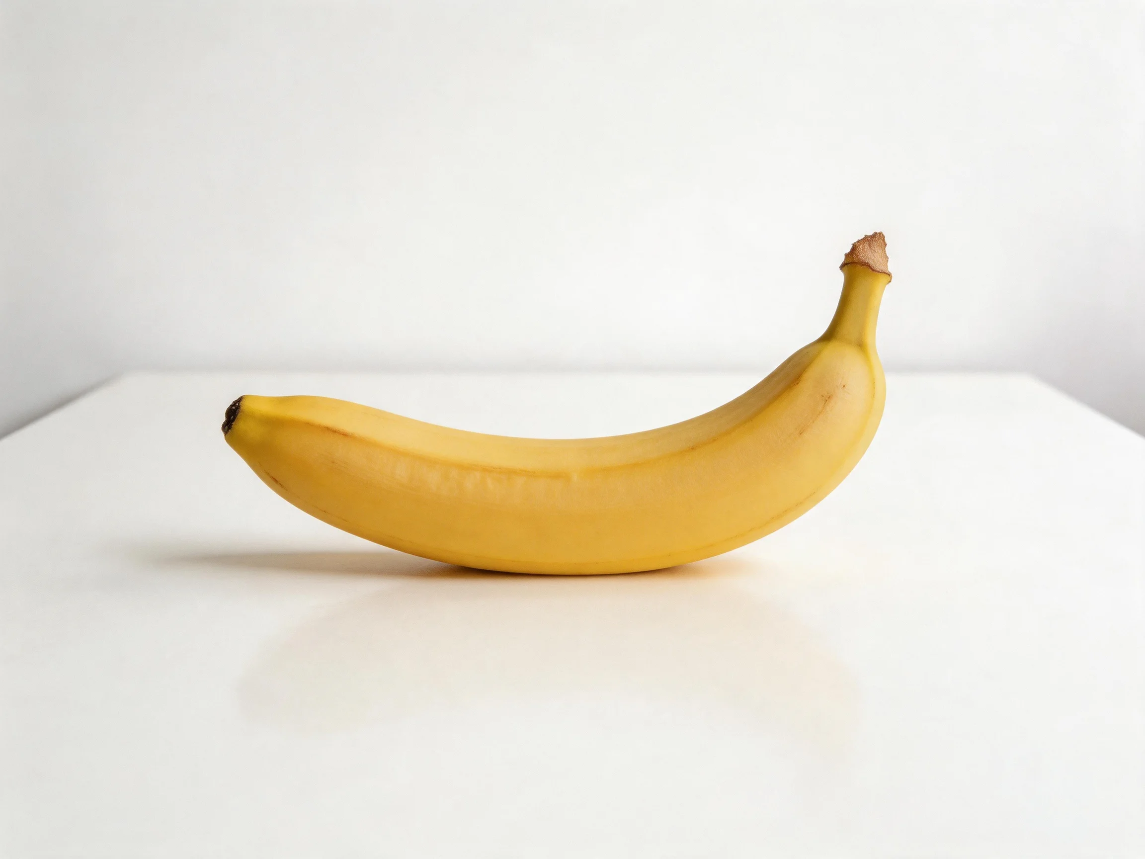 A single ripe yellow banana resting on a smooth white surface
