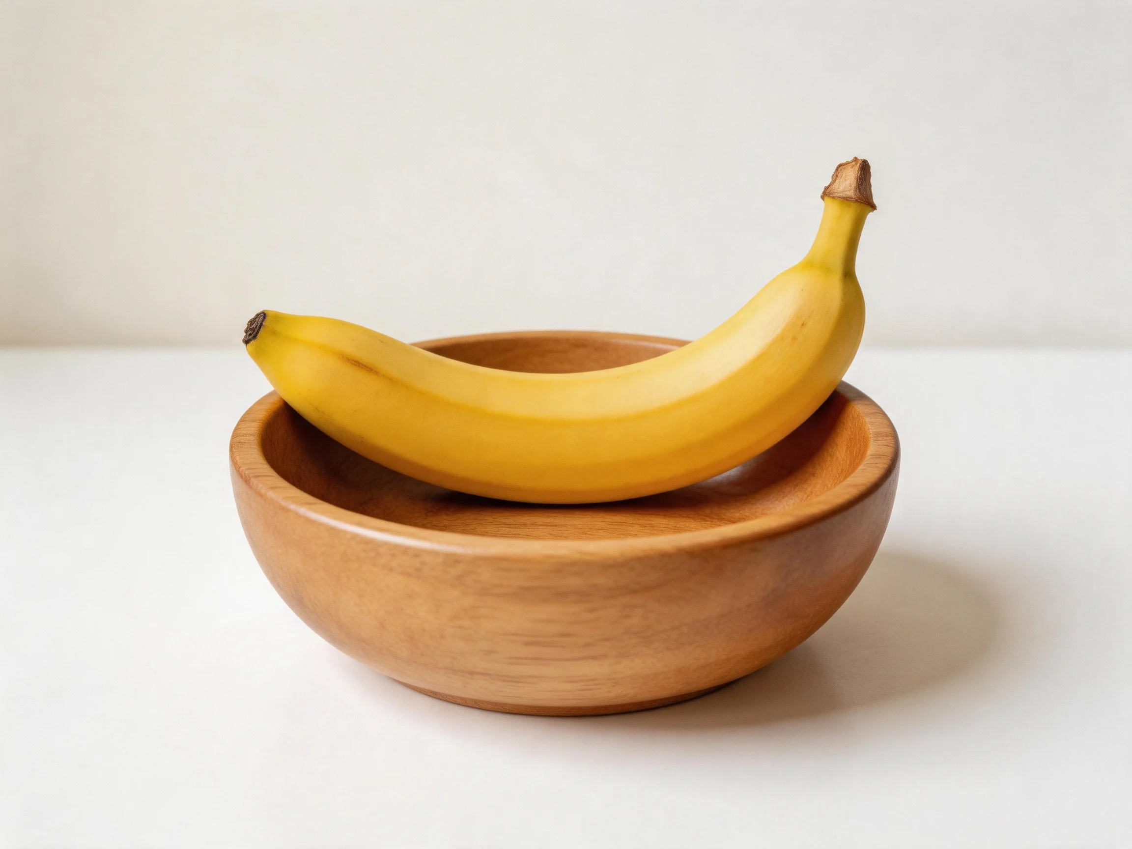 A single ripe yellow banana rests atop a smooth brown wooden bowl