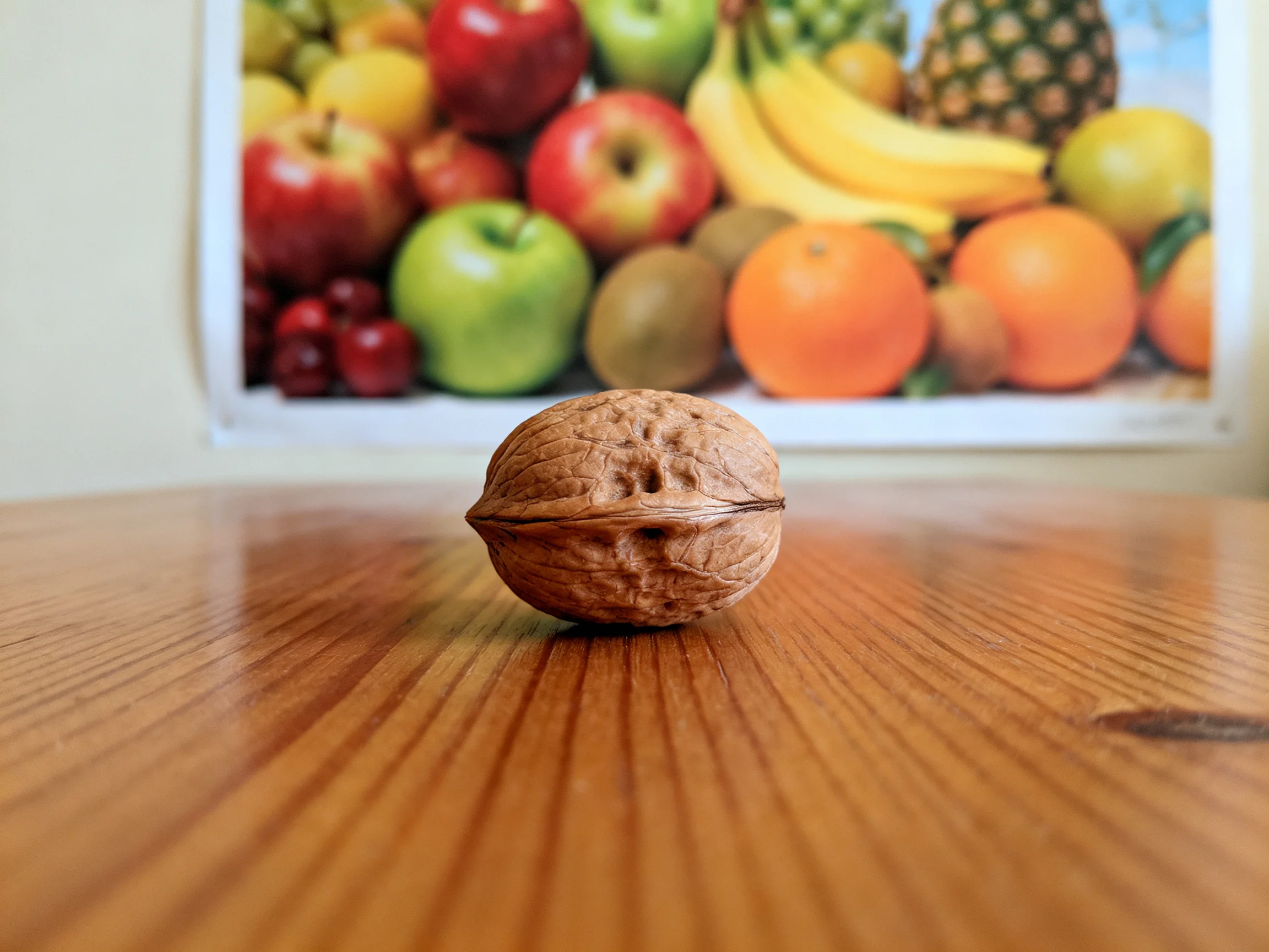 A single walnut sits on polished wood with a colorful fruit poster