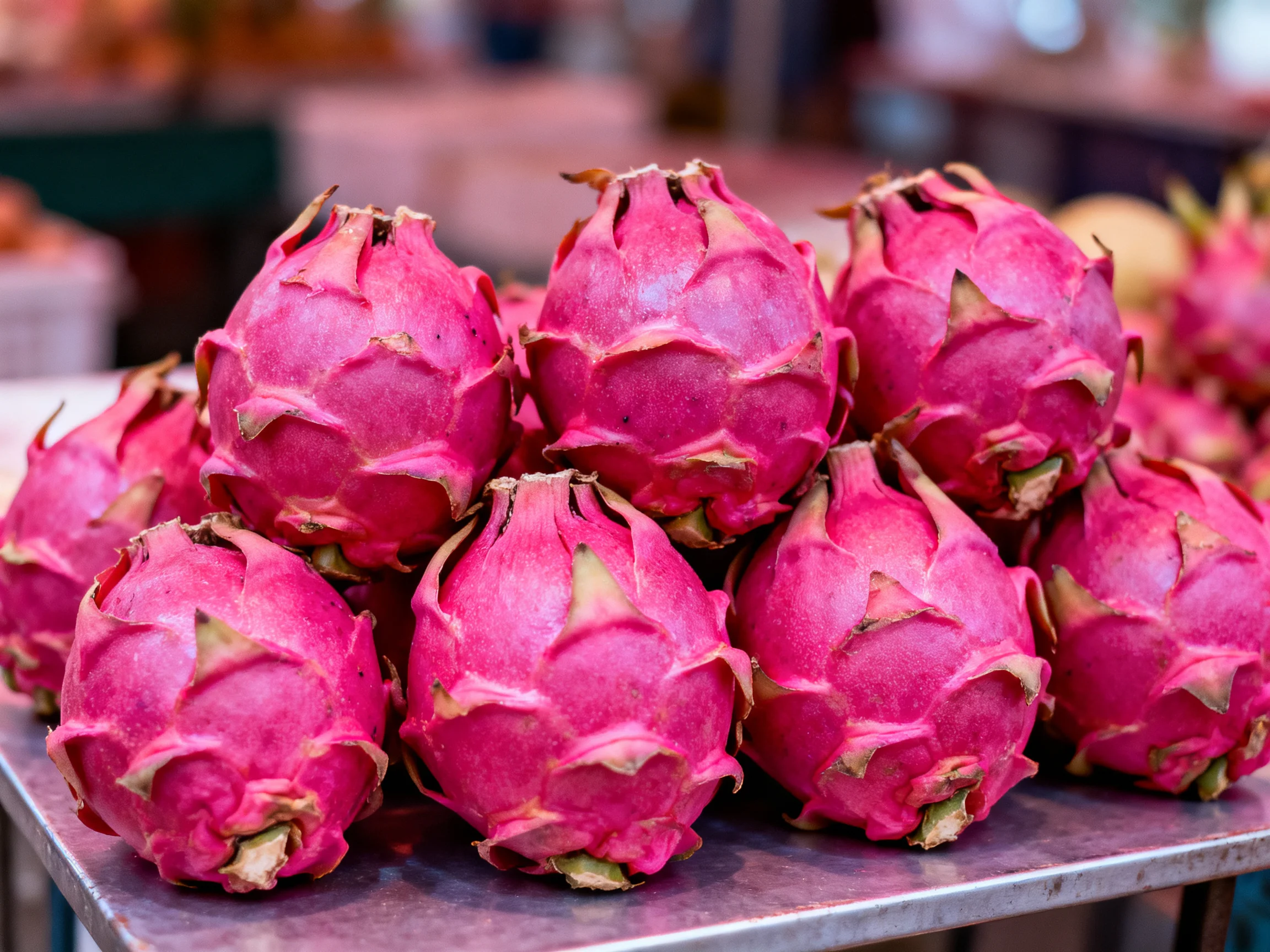 A stack of vibrant pink dragon fruits arranged on a metal surface