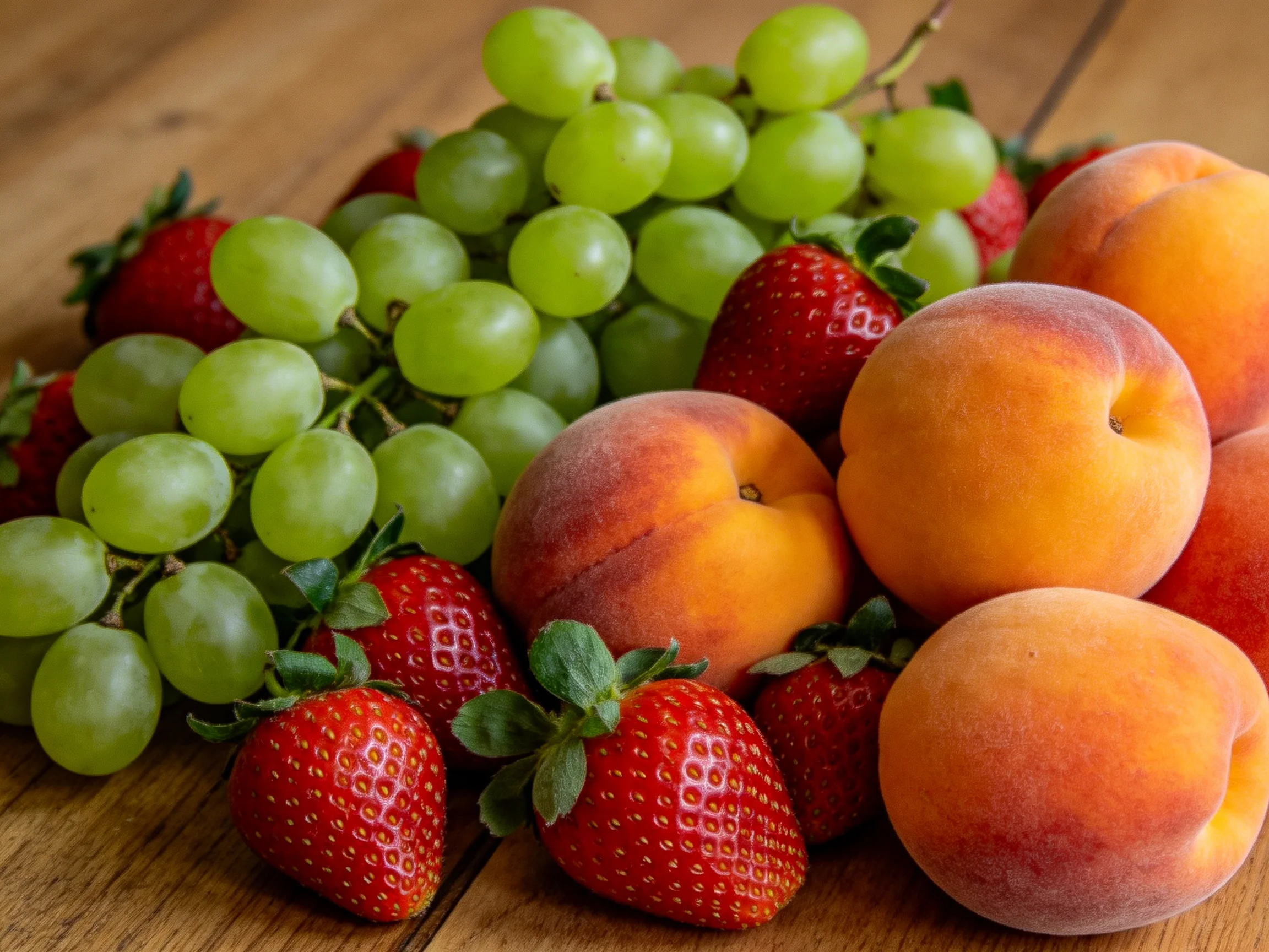 A vibrant arrangement of green grapes, red strawberries, and orange peaches