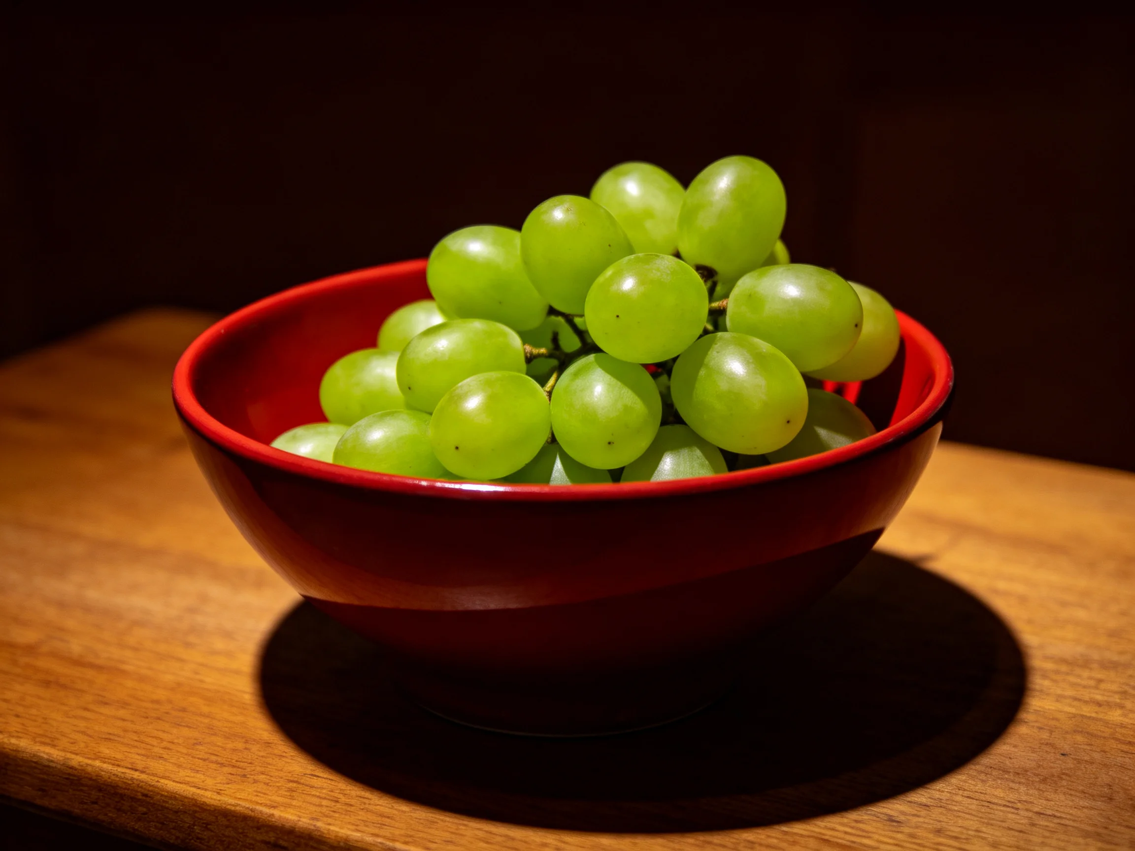A vibrant cluster of green grapes fills a glossy red bowl.