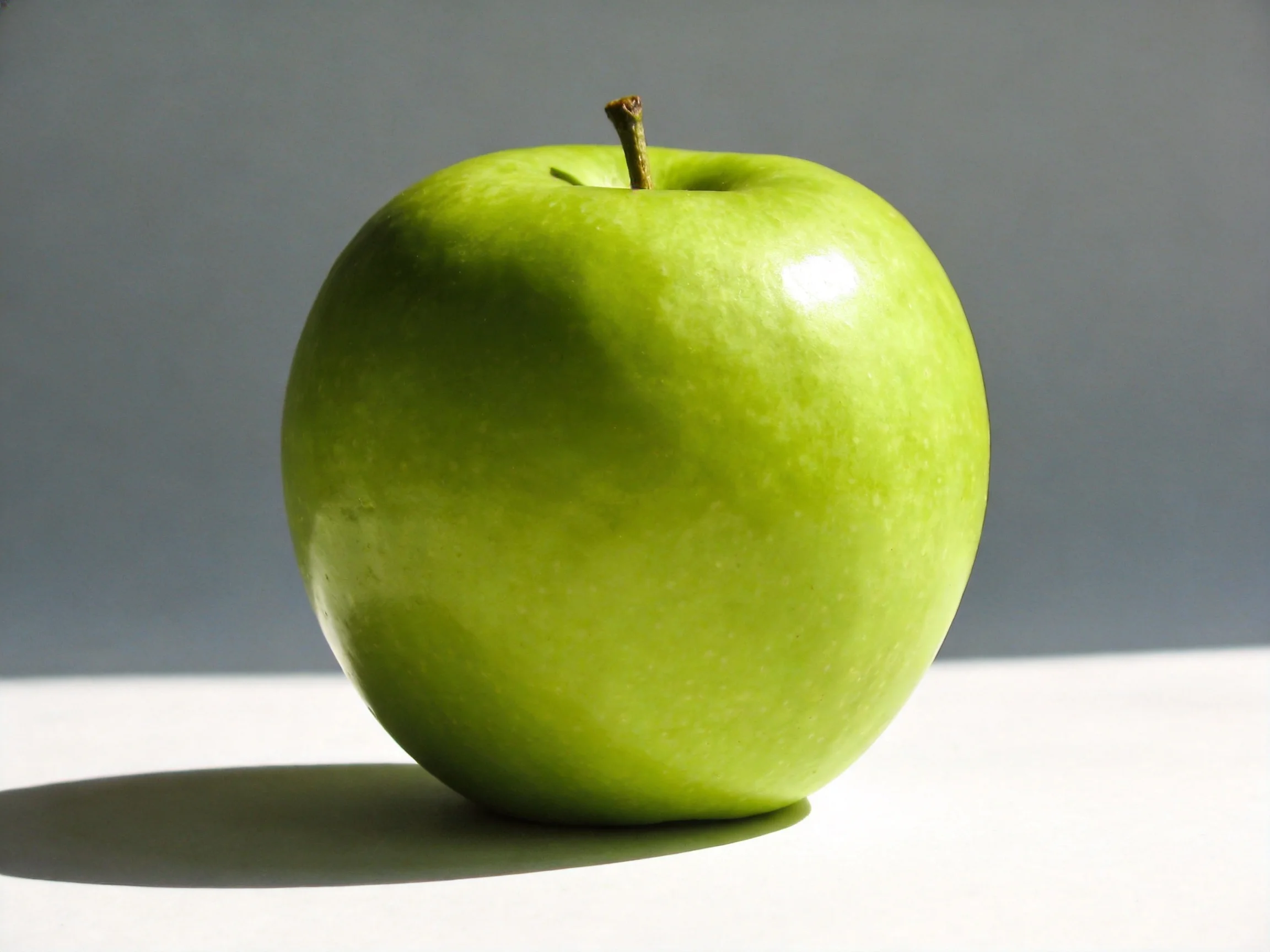 A vibrant green apple rests on a white surface with a gray background