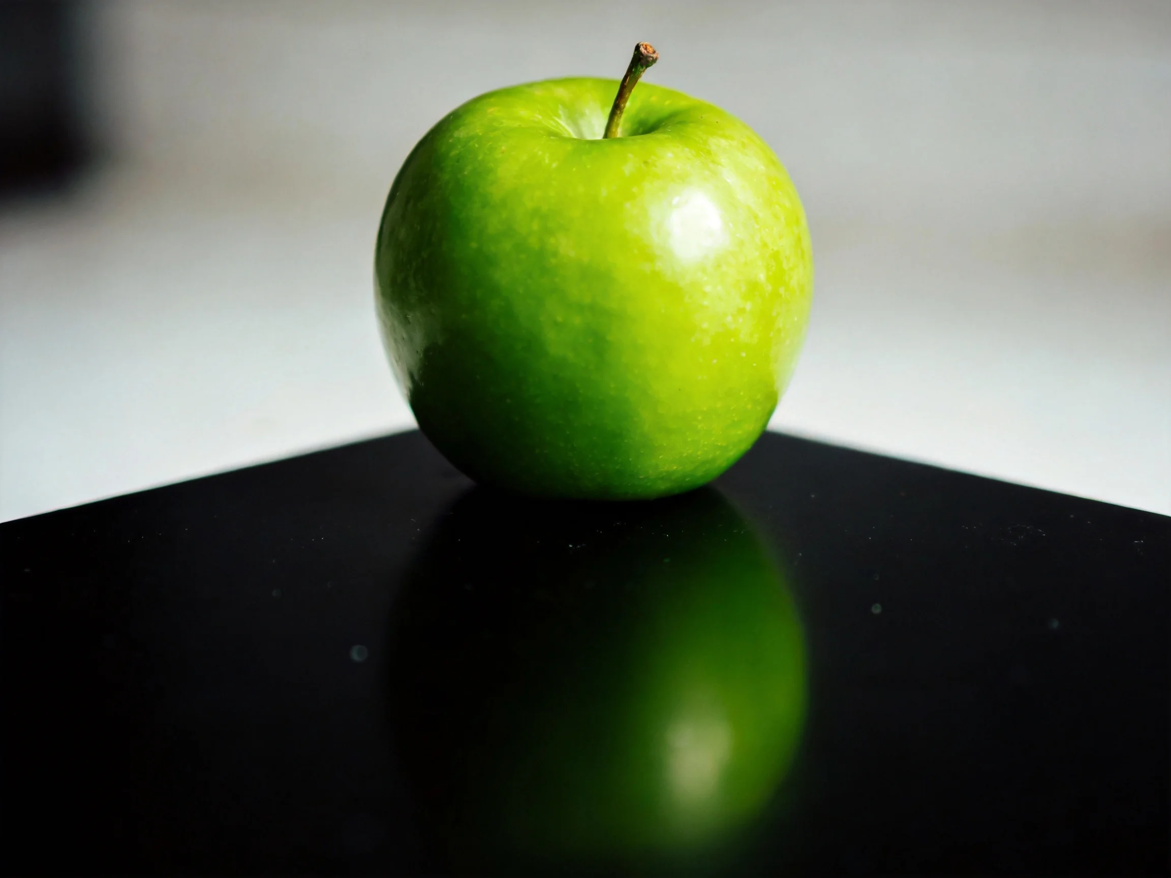 A vibrant green apple sits on a glossy black surface