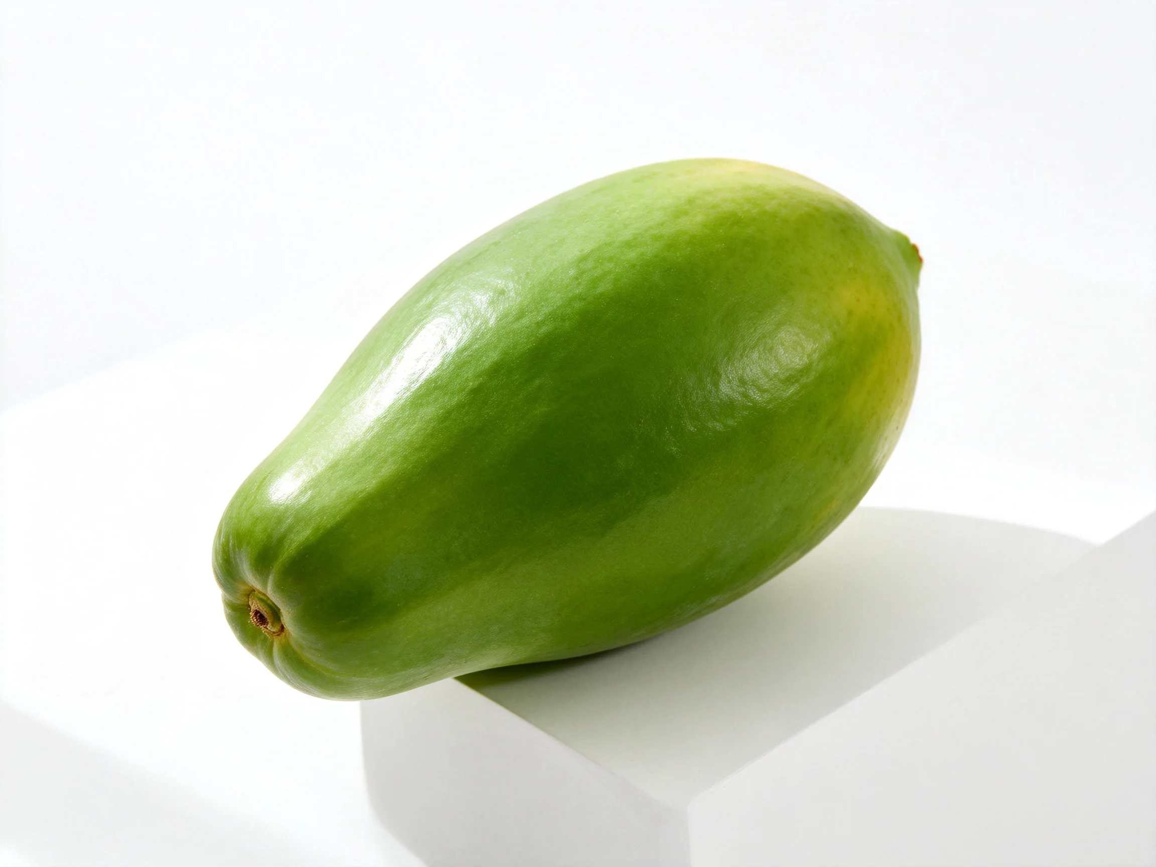 A vibrant green fruit resting on a white geometric block