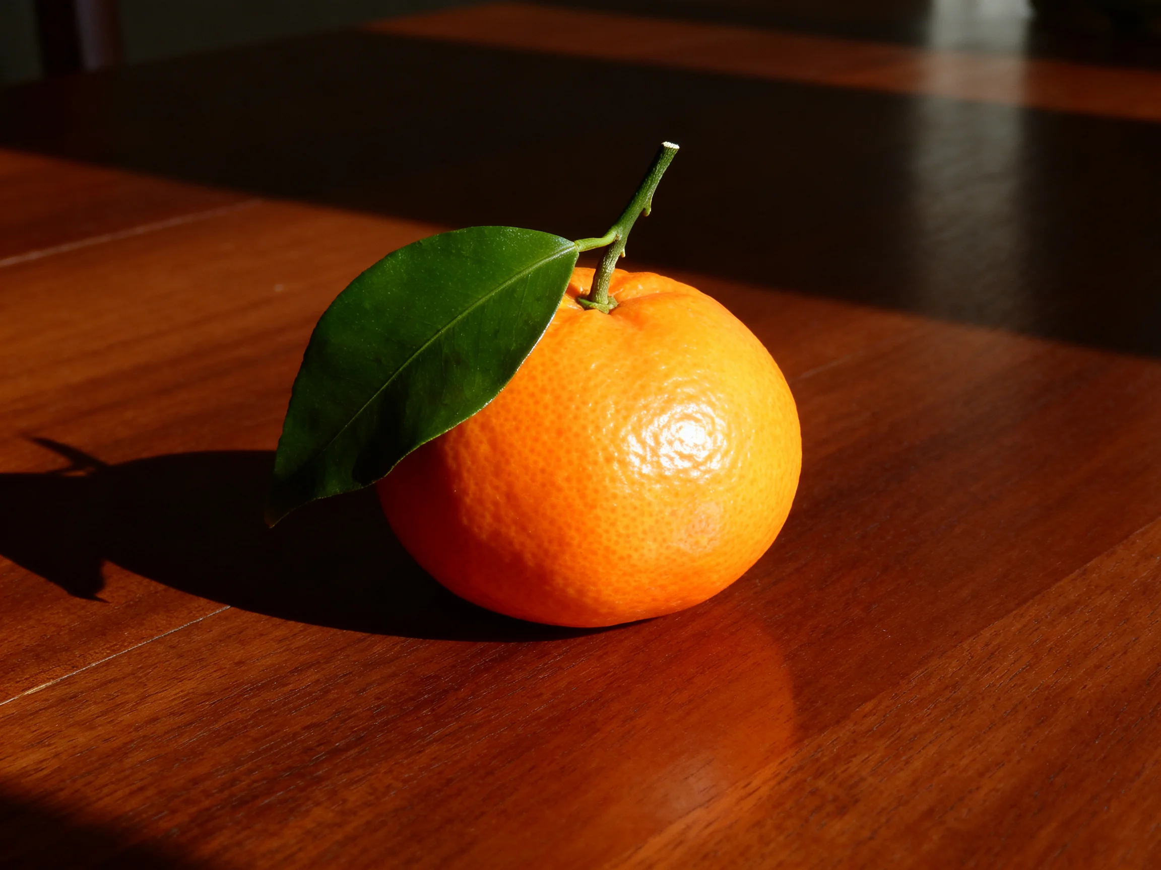 A vibrant orange citrus fruit with a green leaf on a polished wooden table