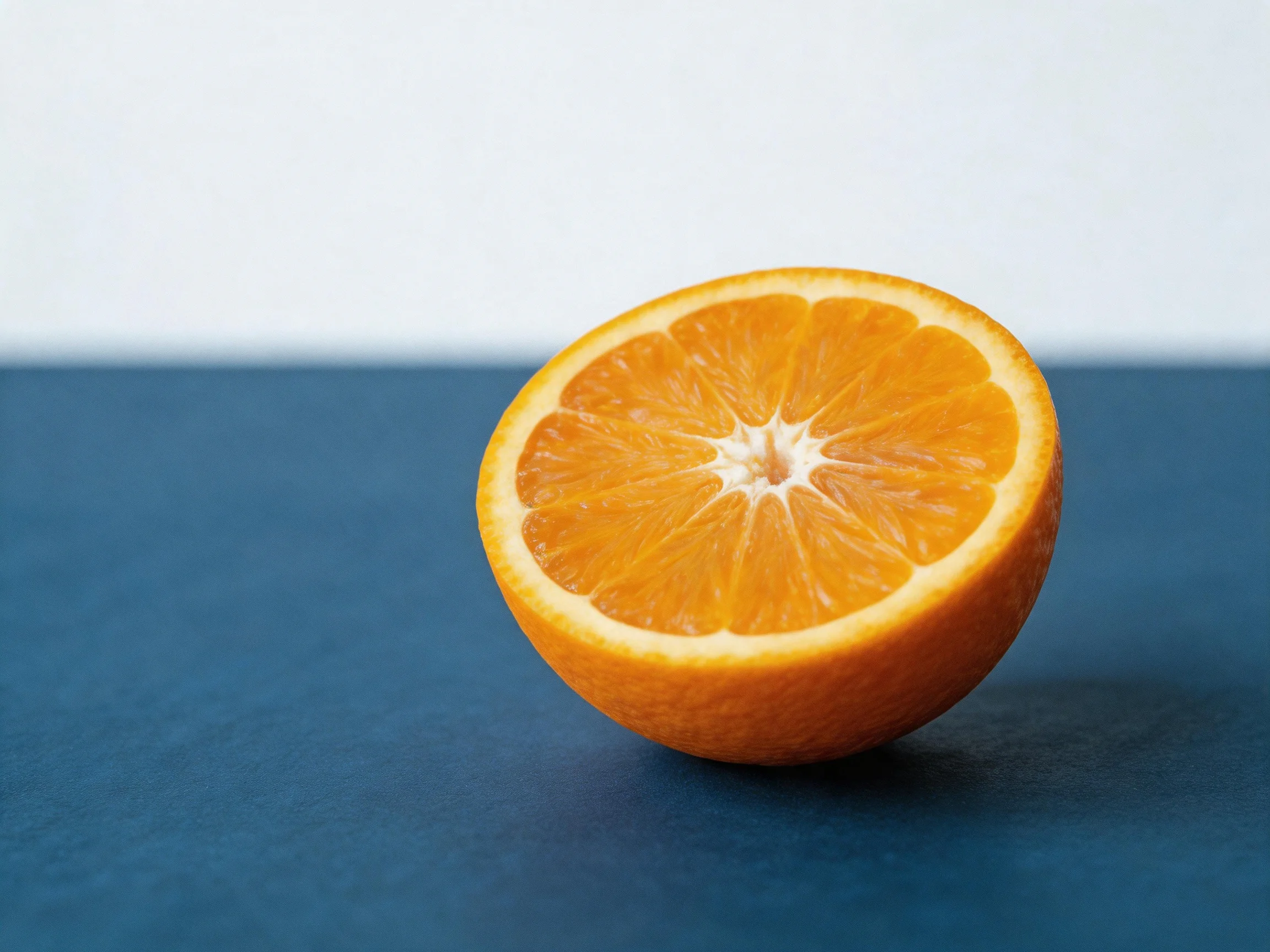 A vibrant orange half resting on a deep blue flat surface