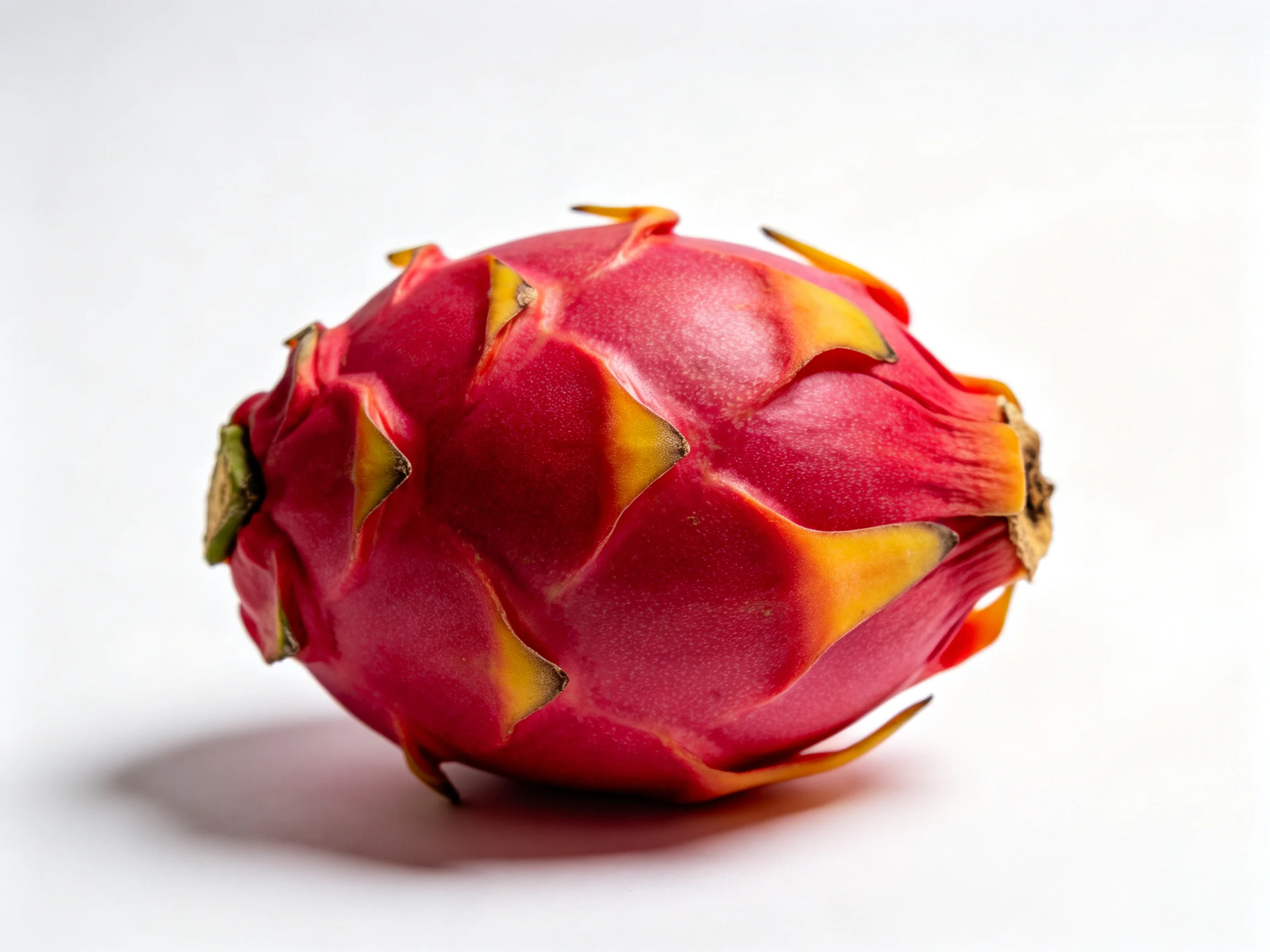 A vibrant red dragon fruit with yellow spiky accents on a plain white backdrop