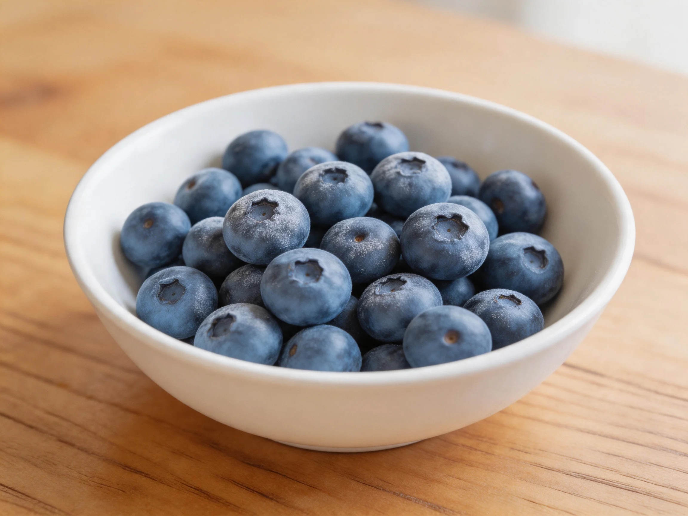 A white bowl brimming with fresh blueberries on a wooden surface