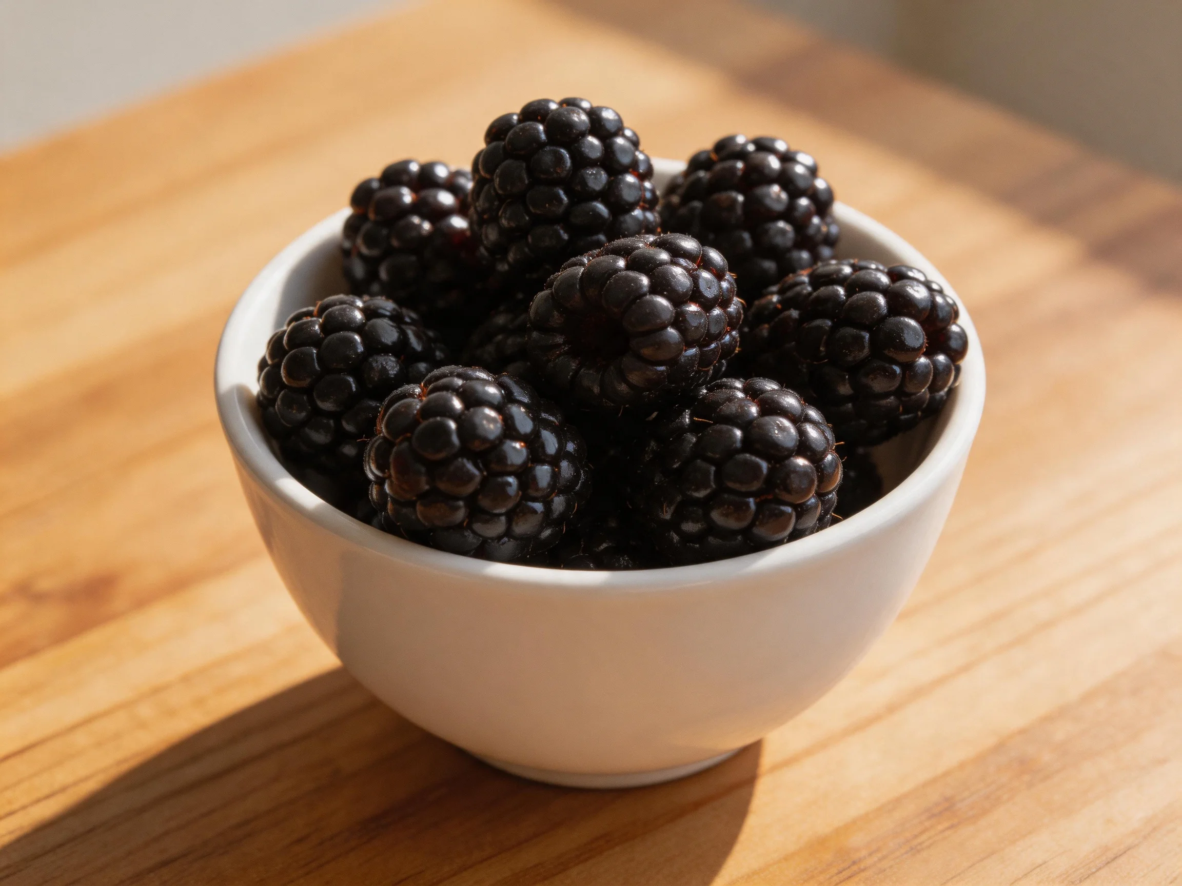 A white bowl brimming with glossy blackberries on a wooden table