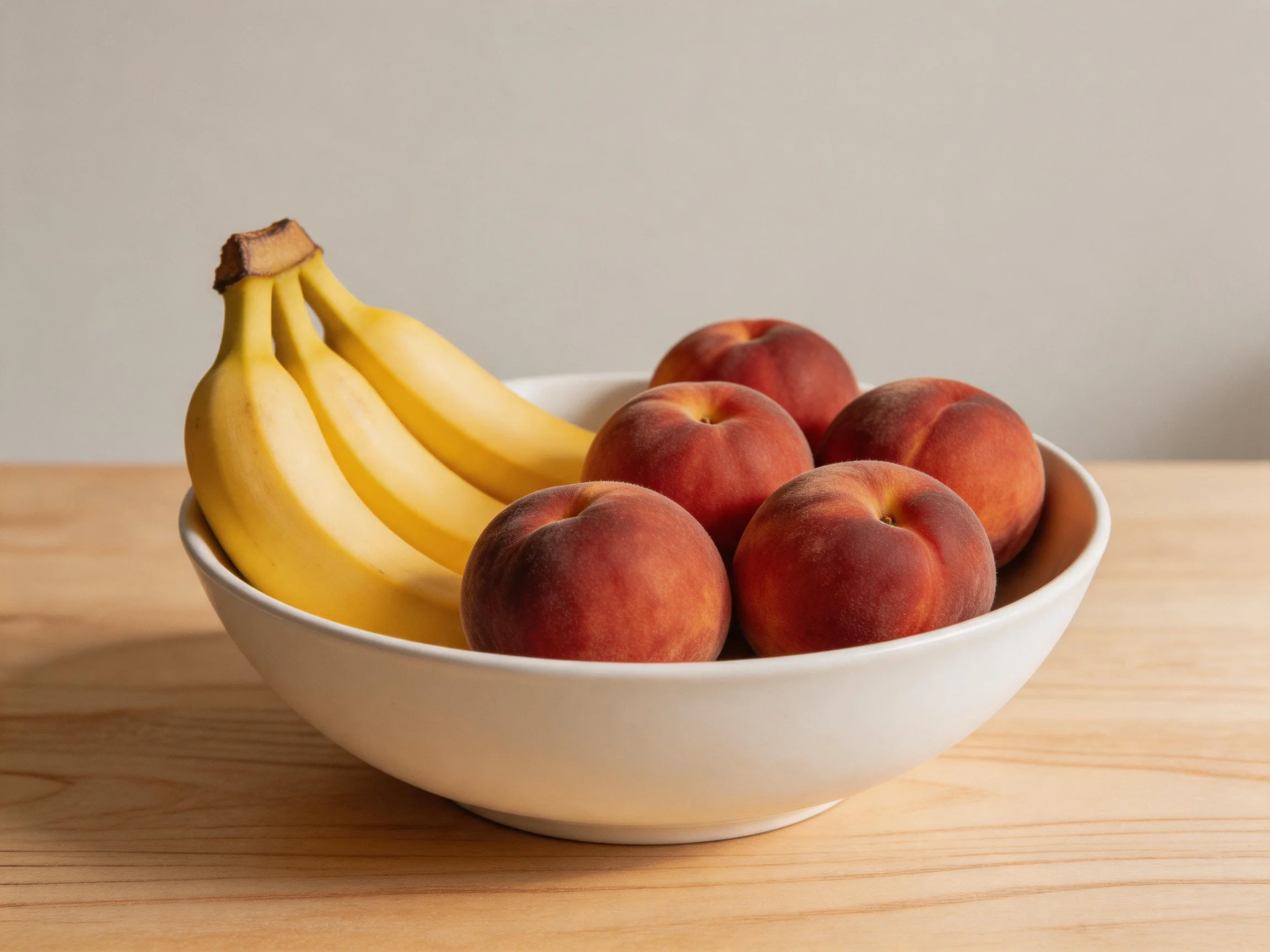 A white bowl holds yellow bananas and reddish-brown peaches