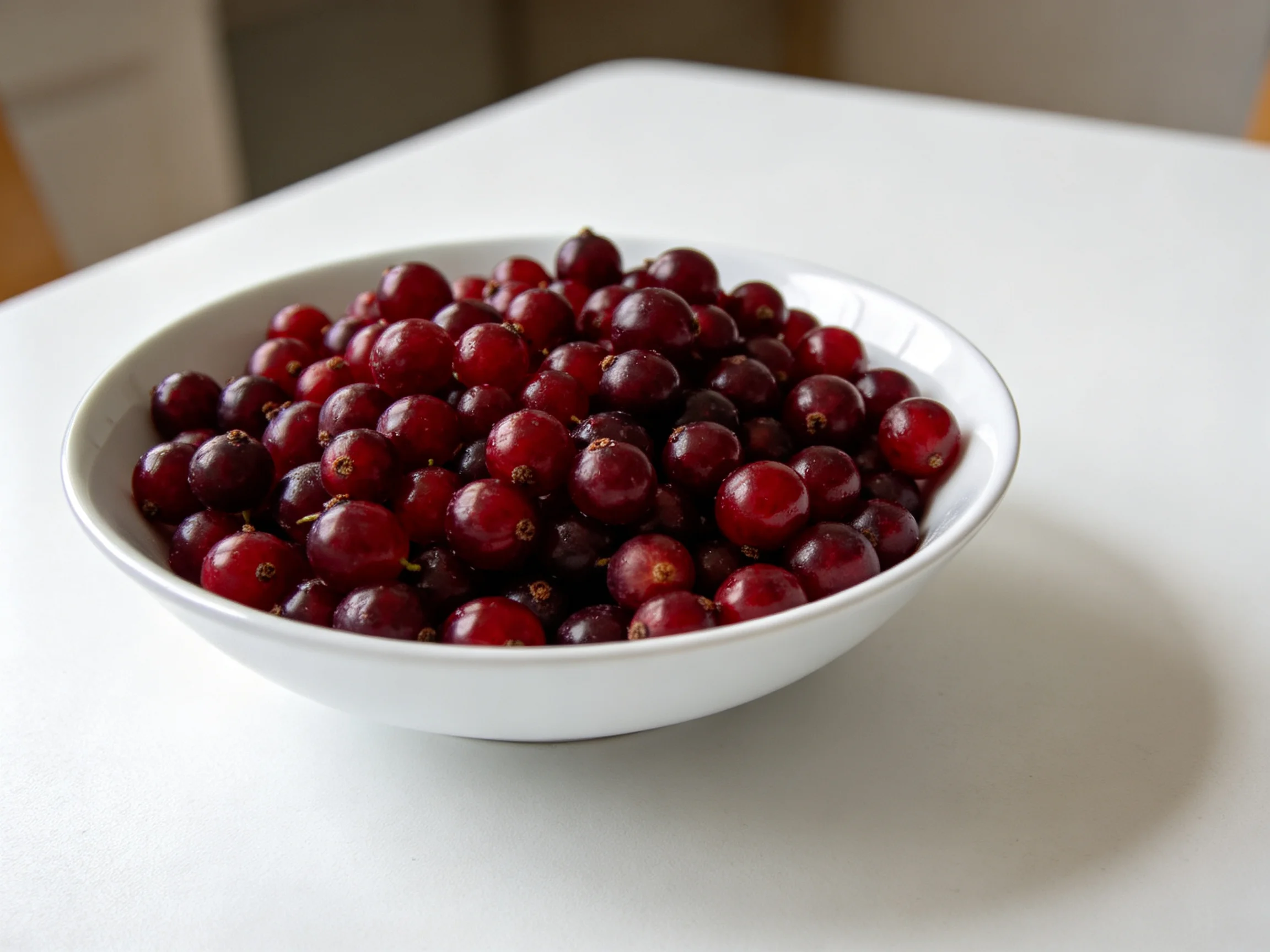 A white bowl overflowed with deep red berries on a smooth table