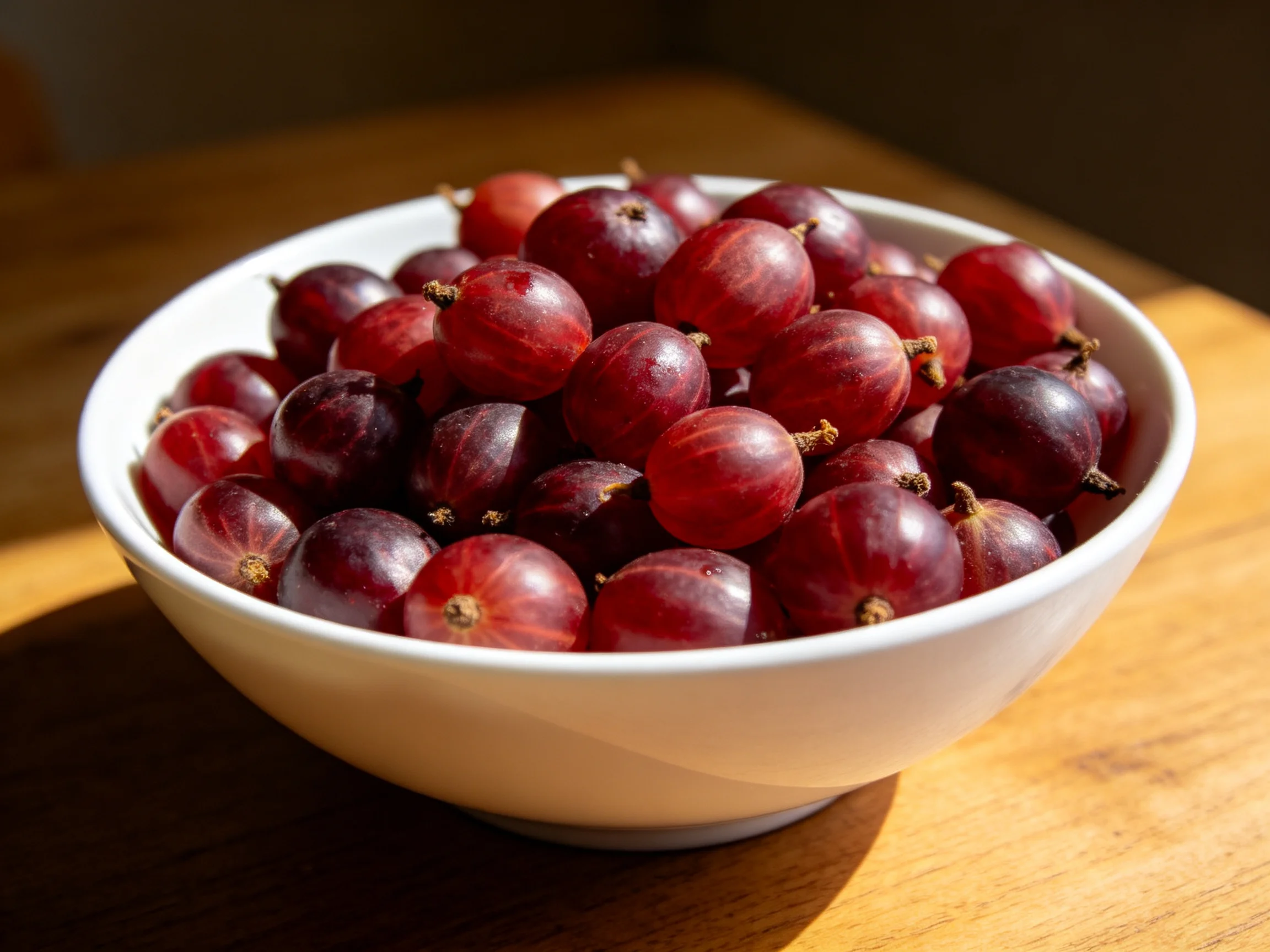 A white bowl overflowing with deep red berries on a wooden table