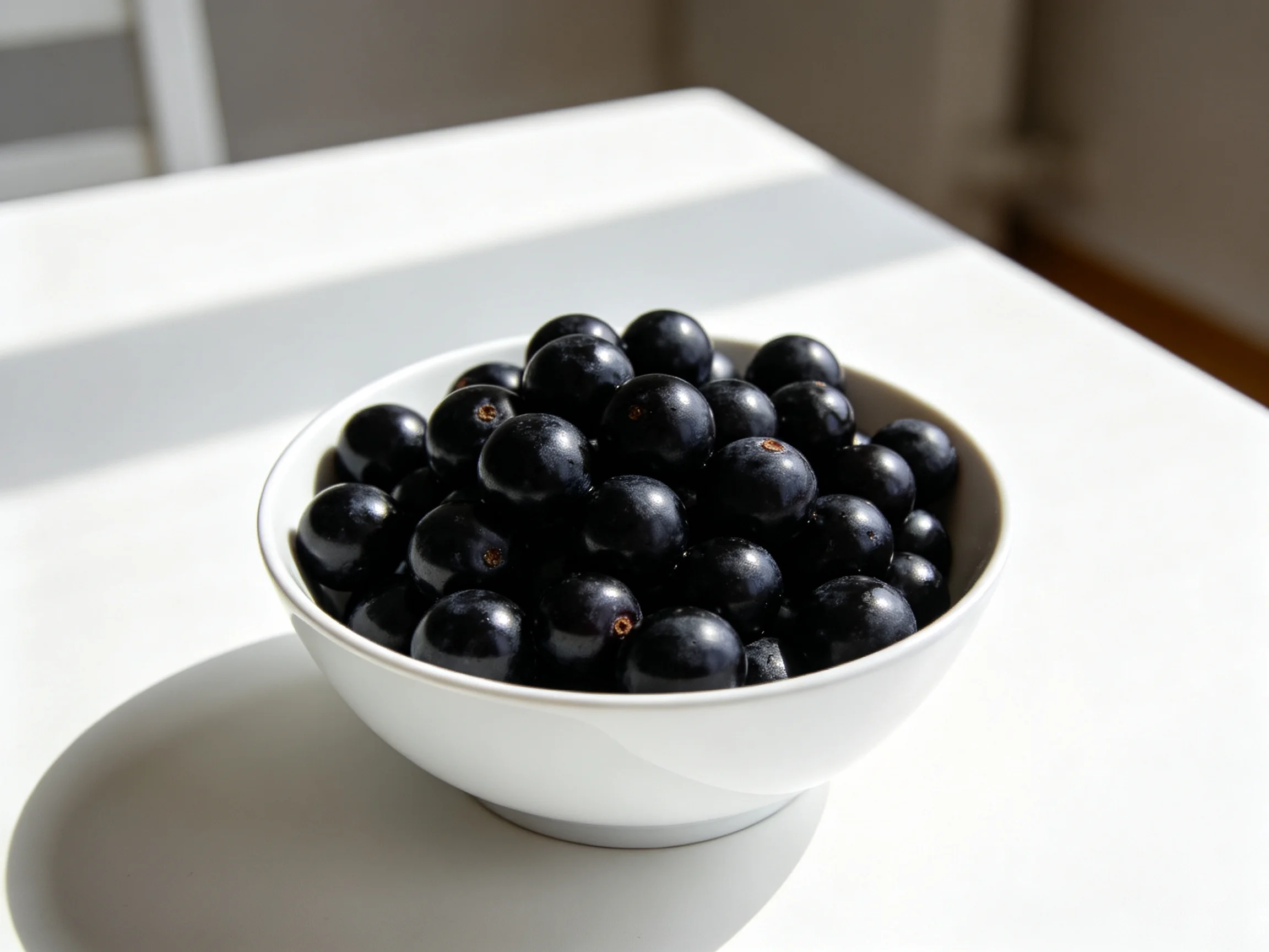 A white bowl overflowing with glossy black berries on a bright table