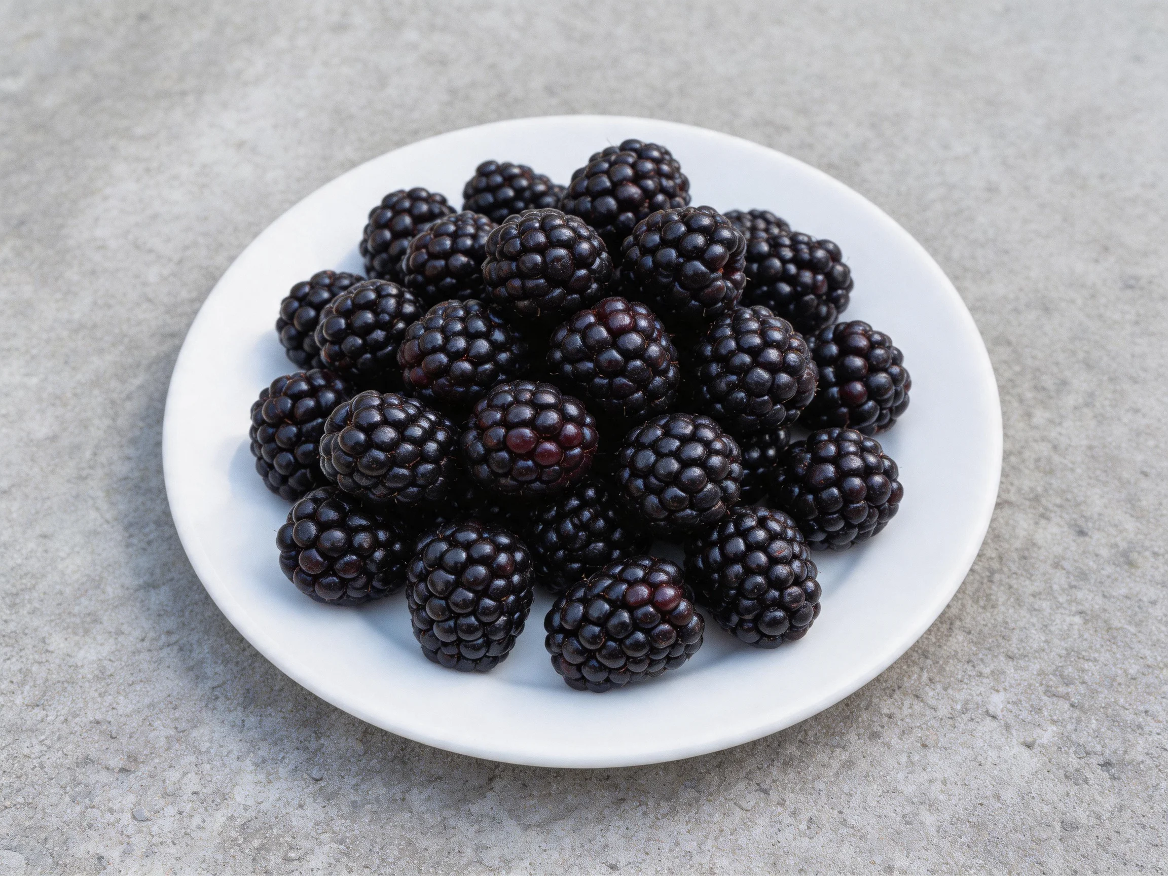 A white plate filled with numerous dark purple blackberries