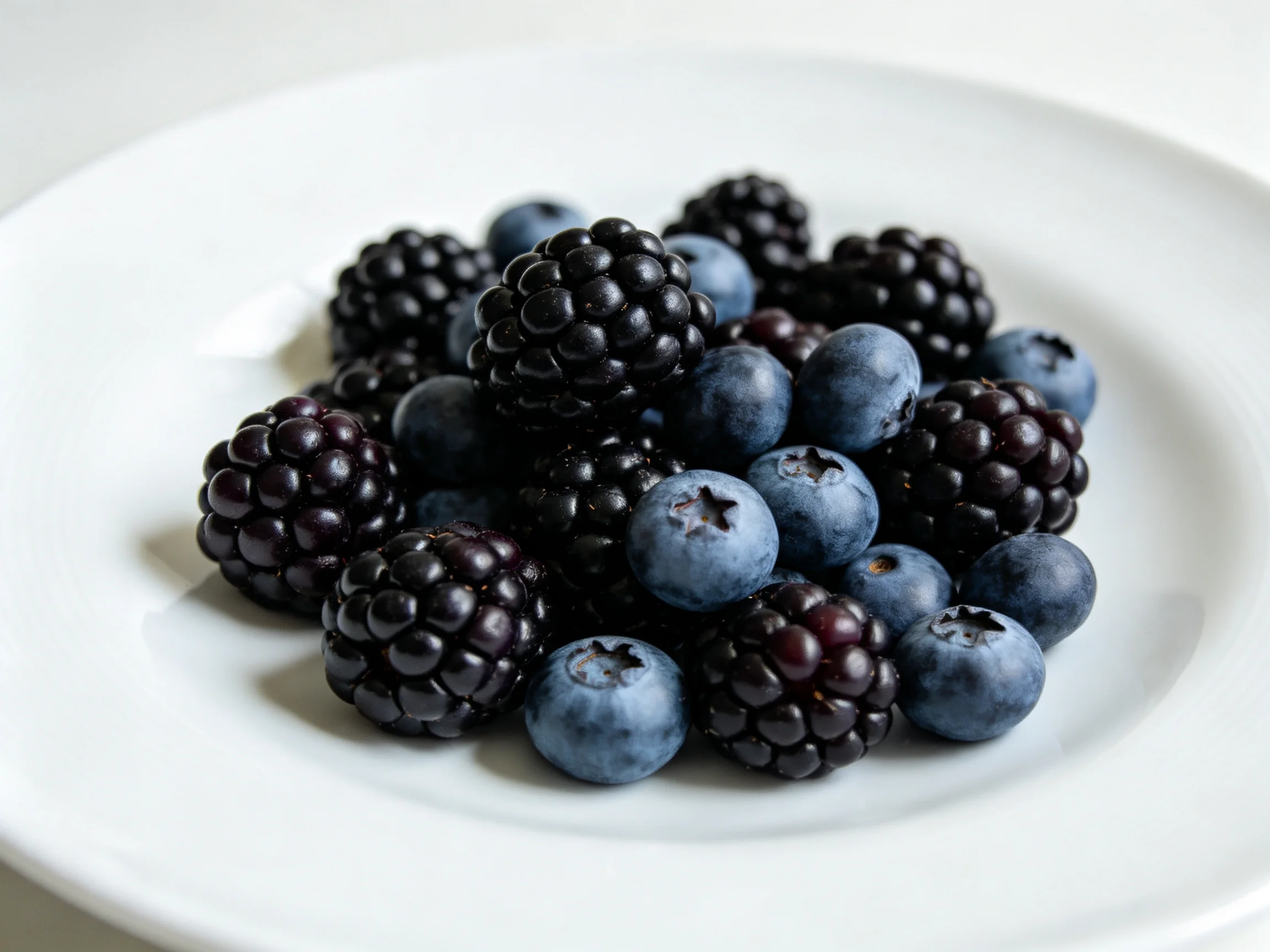 A white plate holds dark blackberries and vibrant blueberries