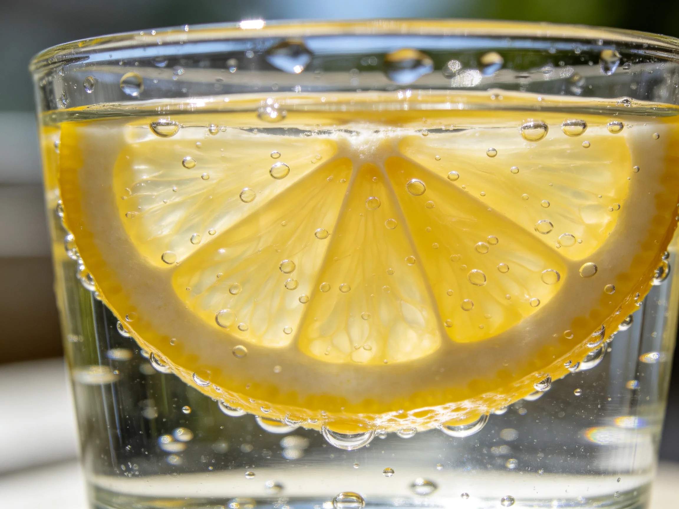 Clear glass holds a lemon slice with rising bubbles