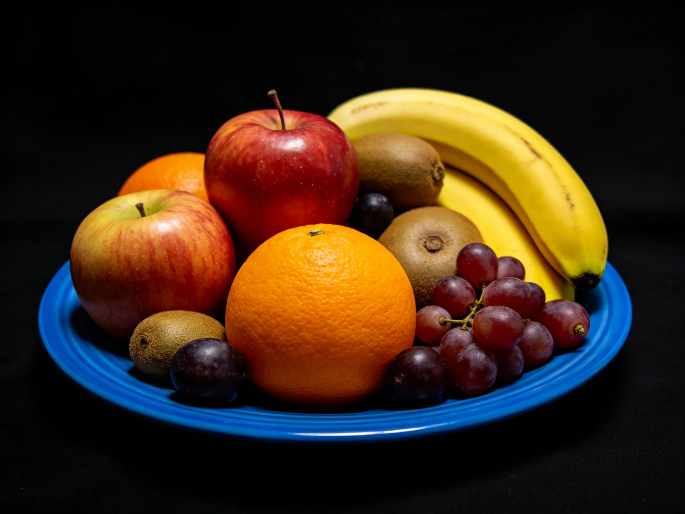 Colorful fruit assortment with apples, bananas, oranges, kiwis, grapes on blue plate