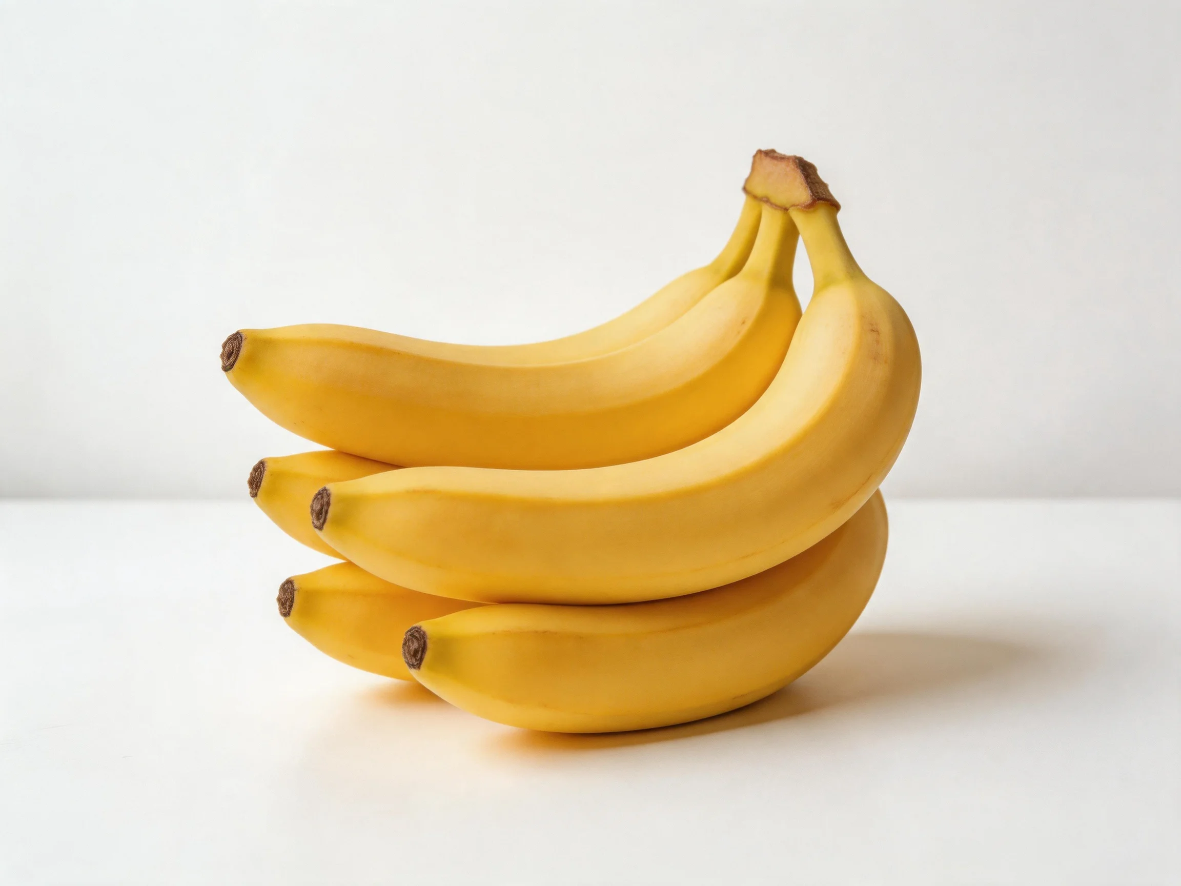 Four bright yellow bananas clustered on a white surface