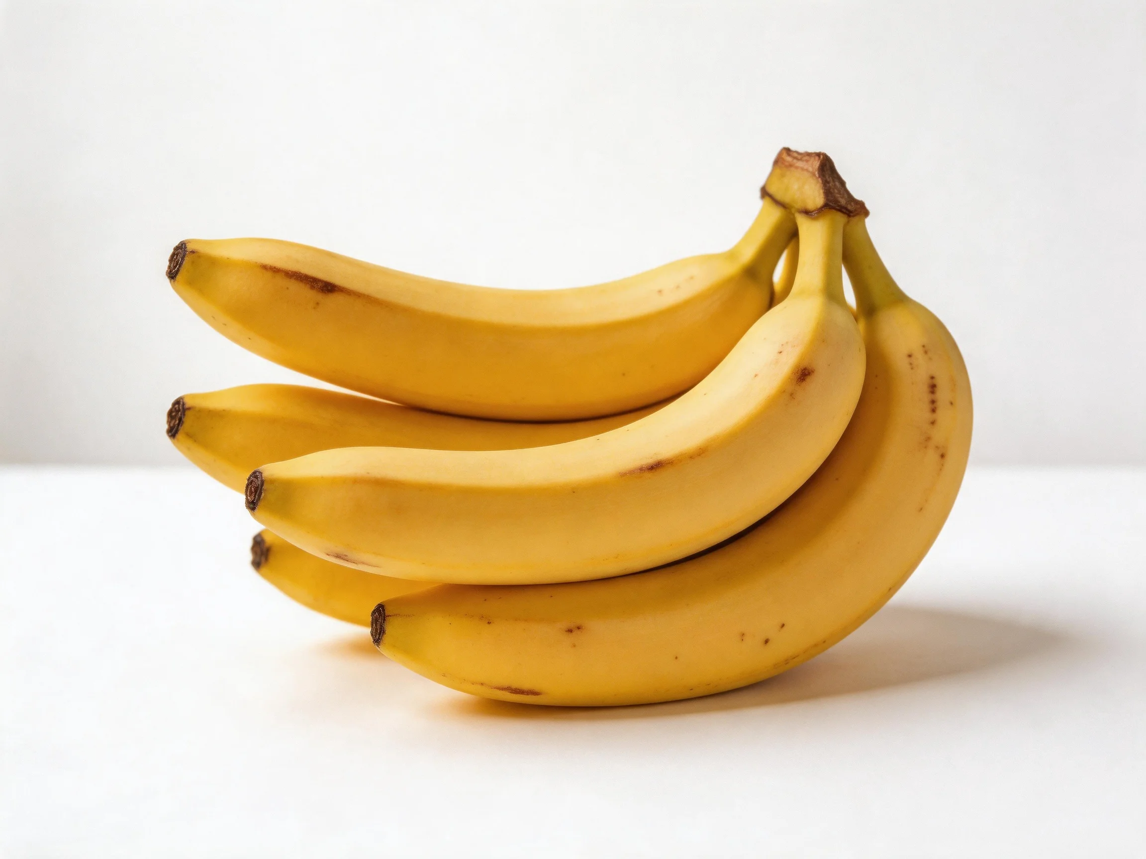 Four ripe yellow bananas clustered on a white surface