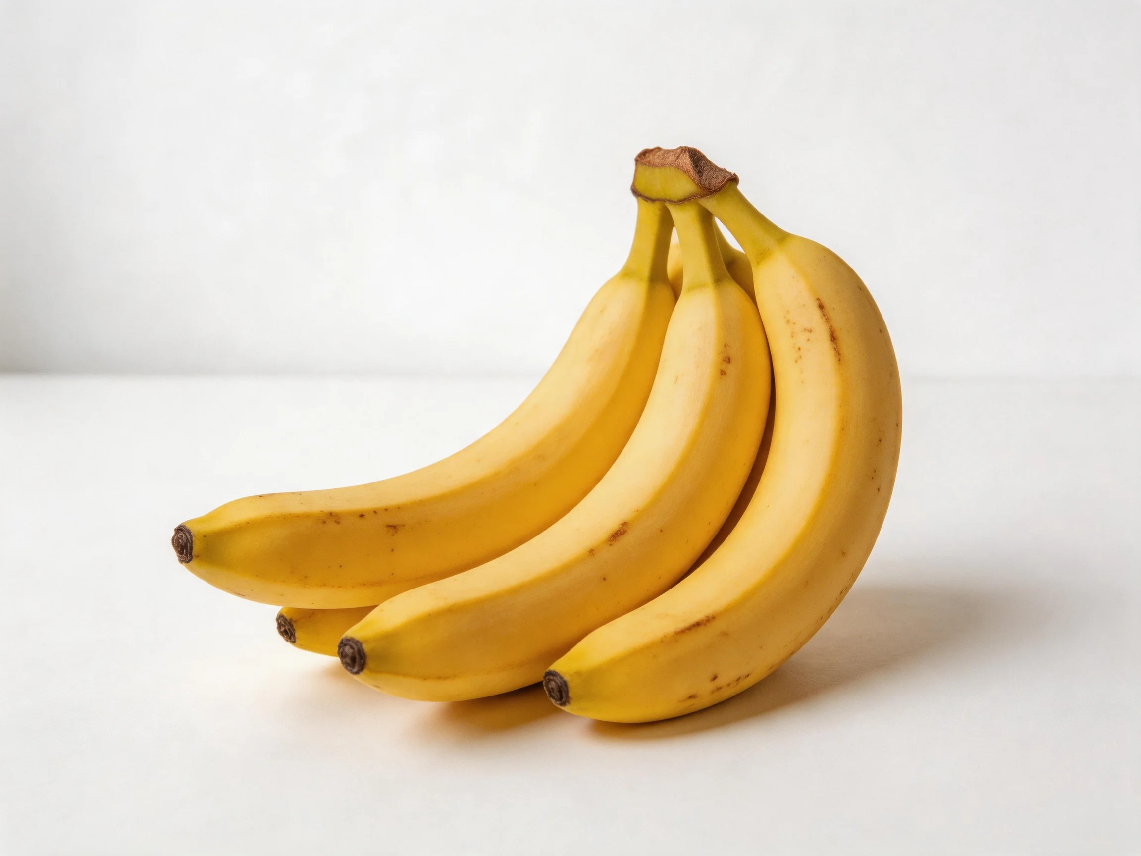 Four ripe yellow bananas clustered together on a plain white surface