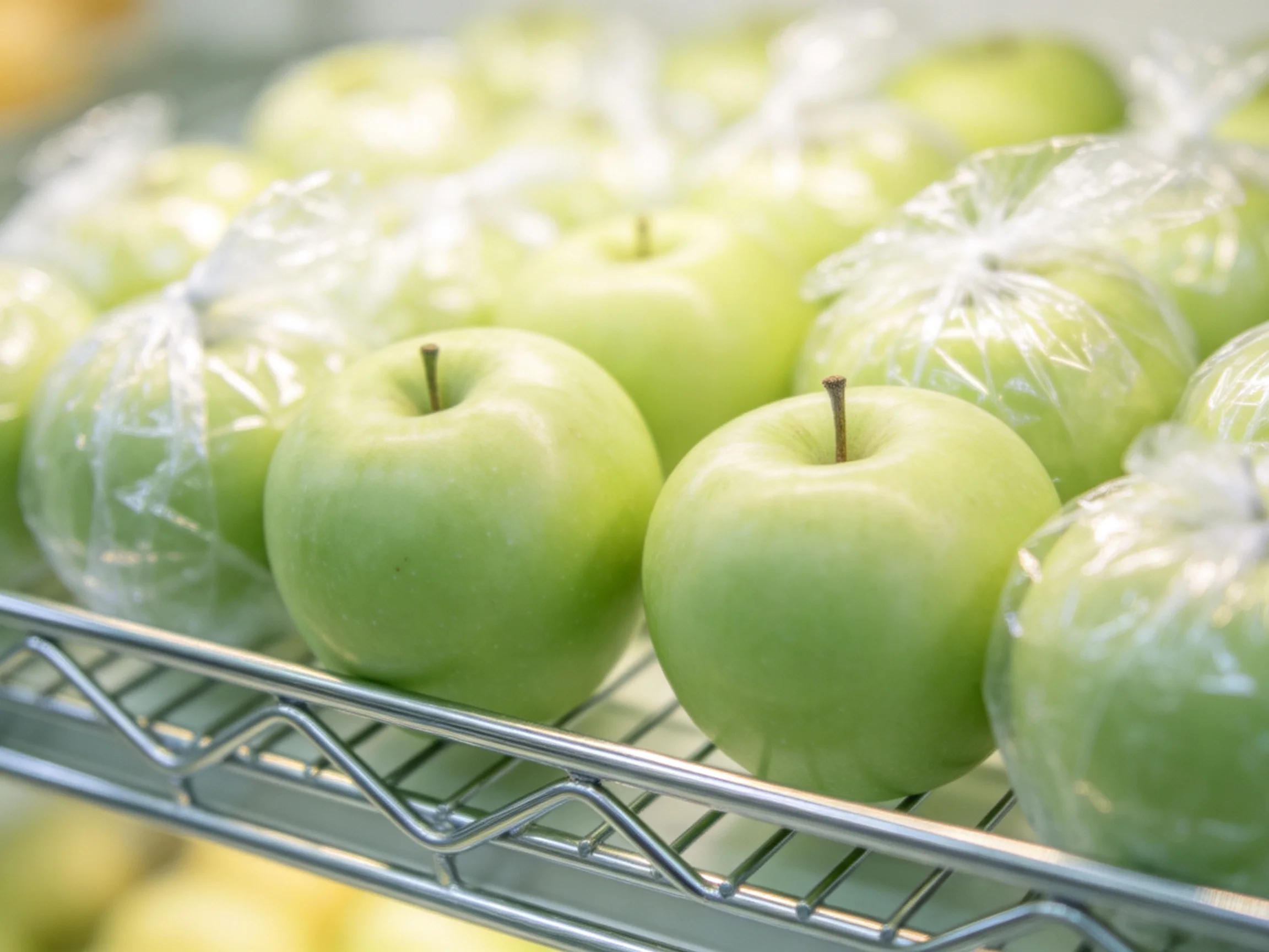 Fresh green apples wrapped in plastic on a metal rack