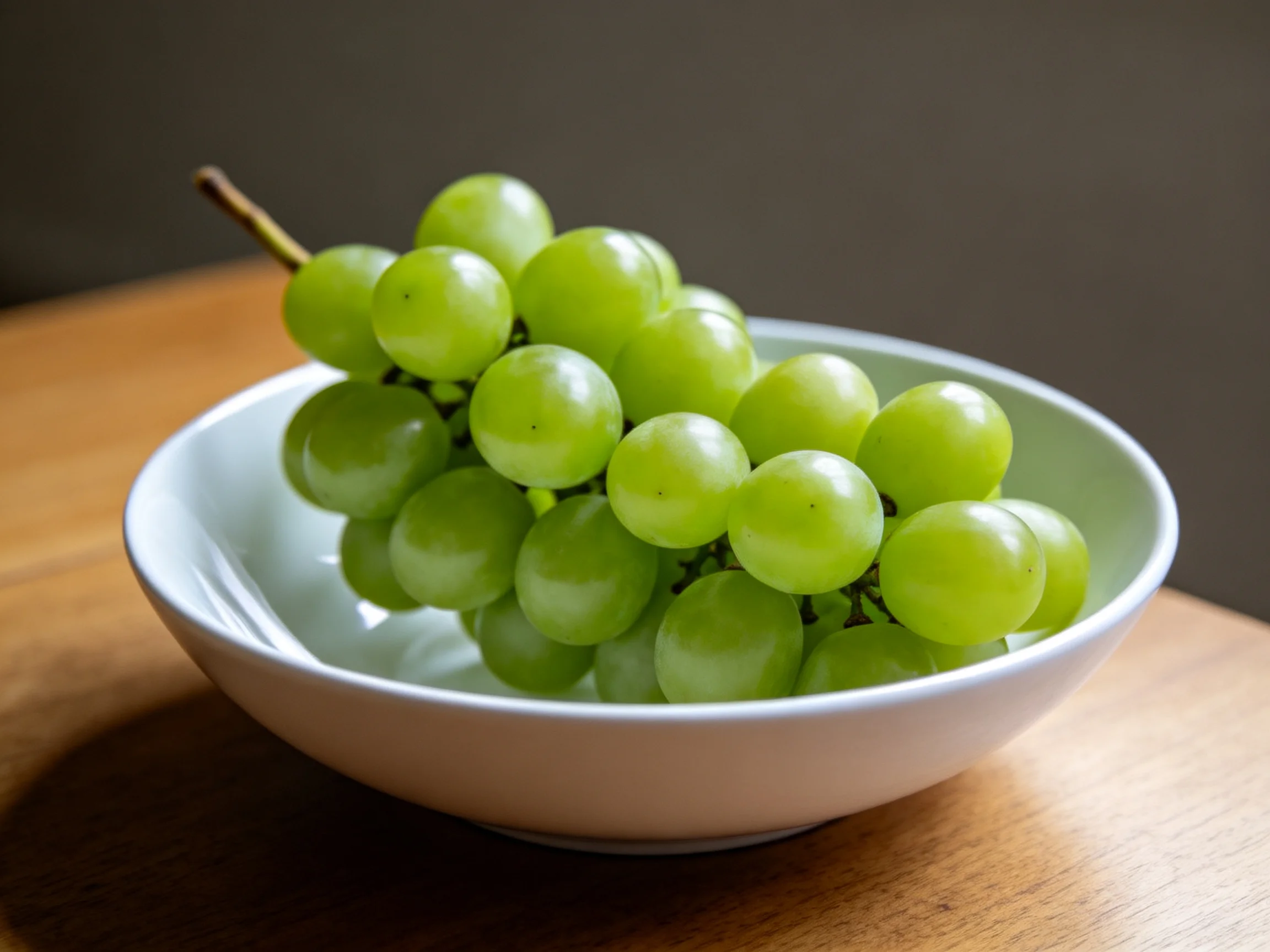 Fresh green grapes clustered in a white bowl on a wooden table