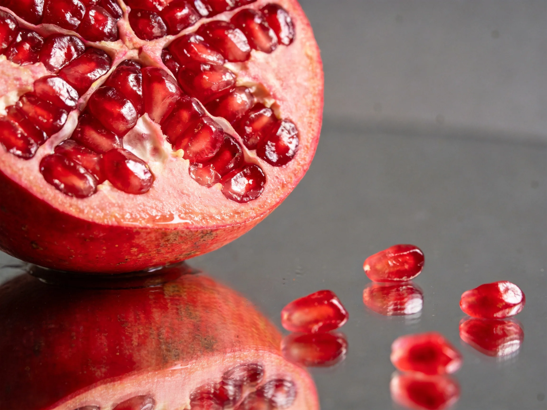 Halved pomegranate with scattered seeds on reflective surface