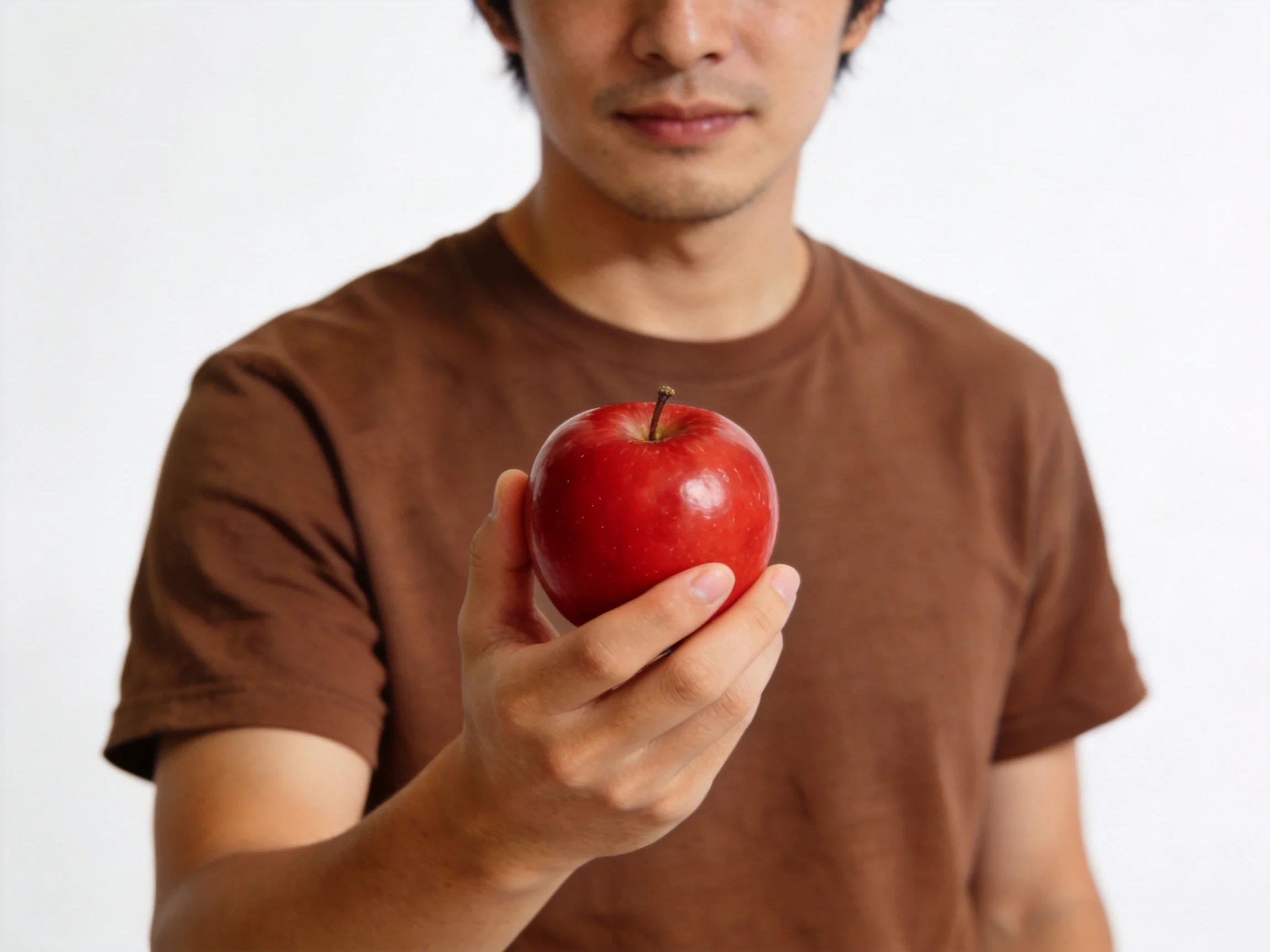 Person in brown shirt presents a glossy red apple