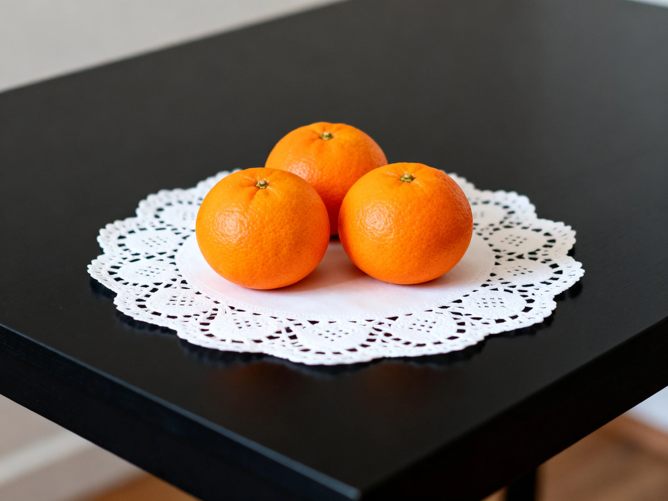 Three bright orange fruits sit on a white lace doily atop a glossy black table