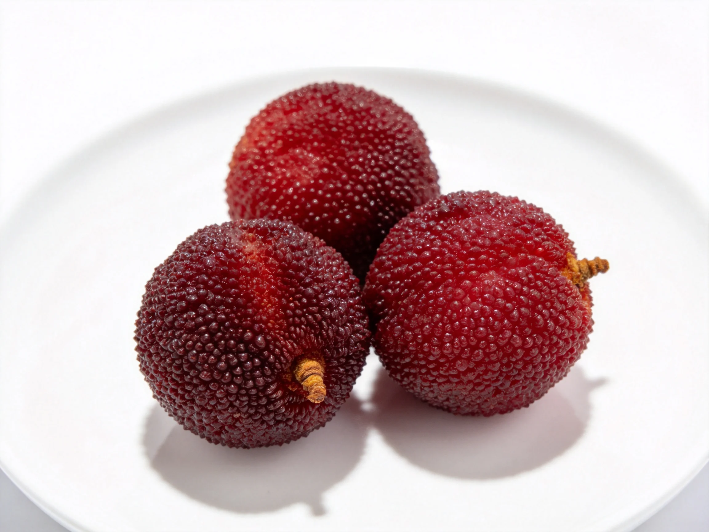 Three glossy dark red round fruits on a white plate