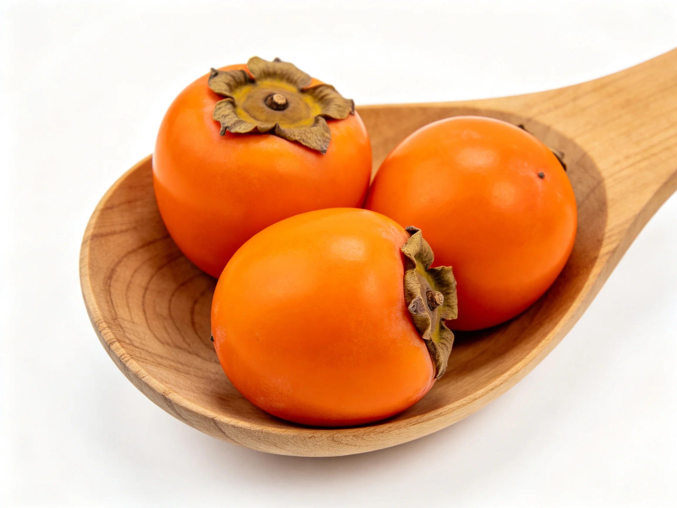 Three glossy orange persimmons in a wooden spoon
