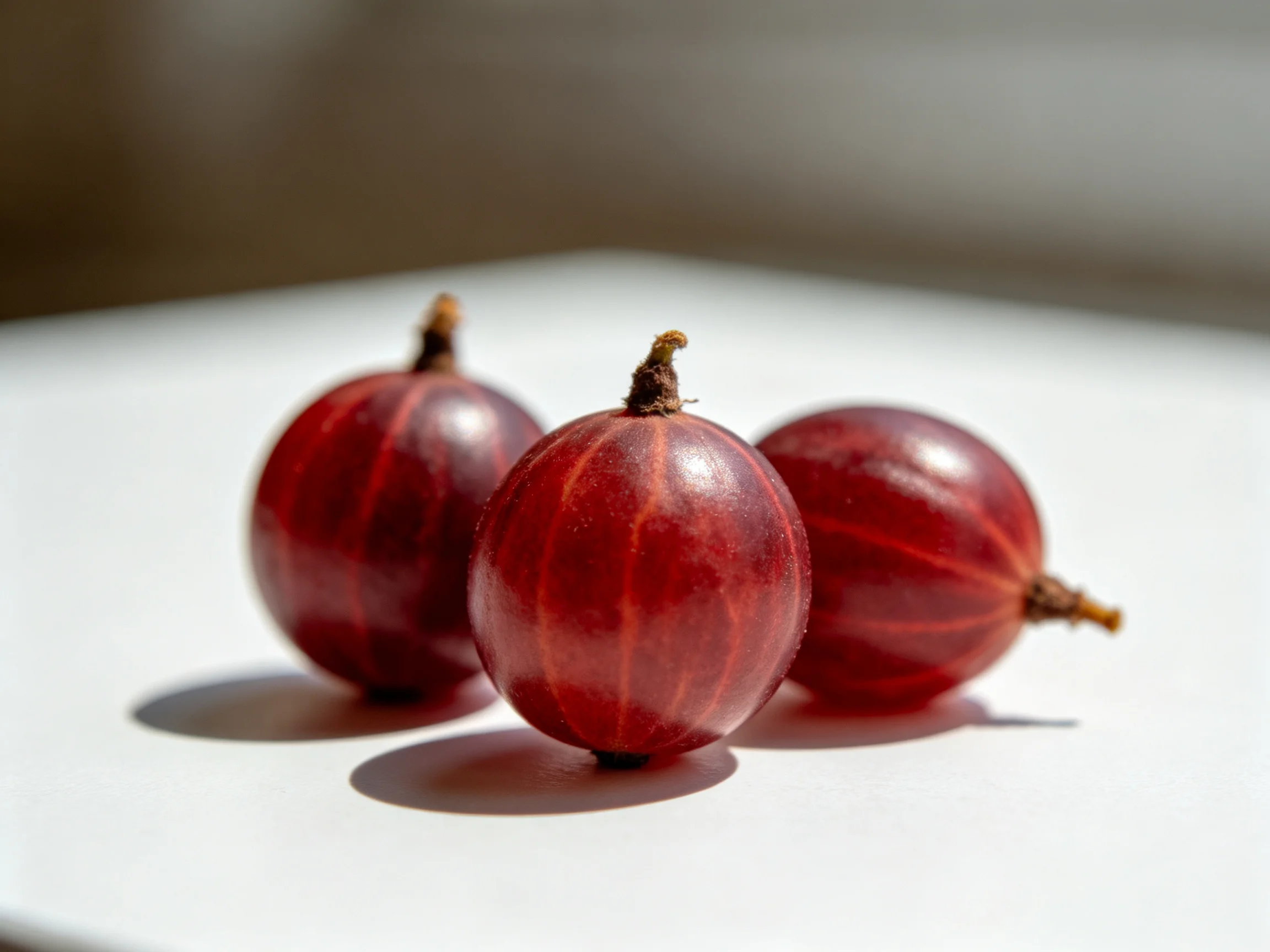 Three glossy red berries arranged on a white surface