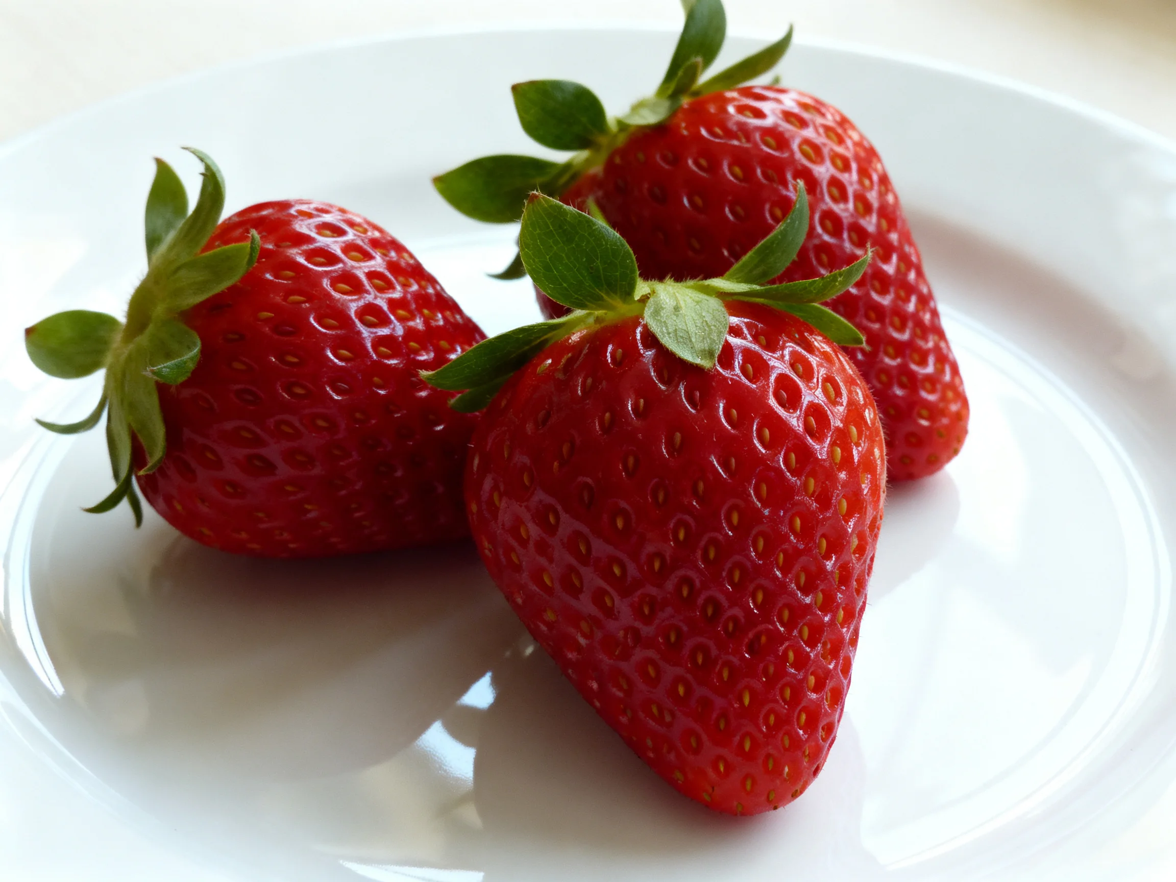 Three plump red strawberries with fresh green stems on a white dish