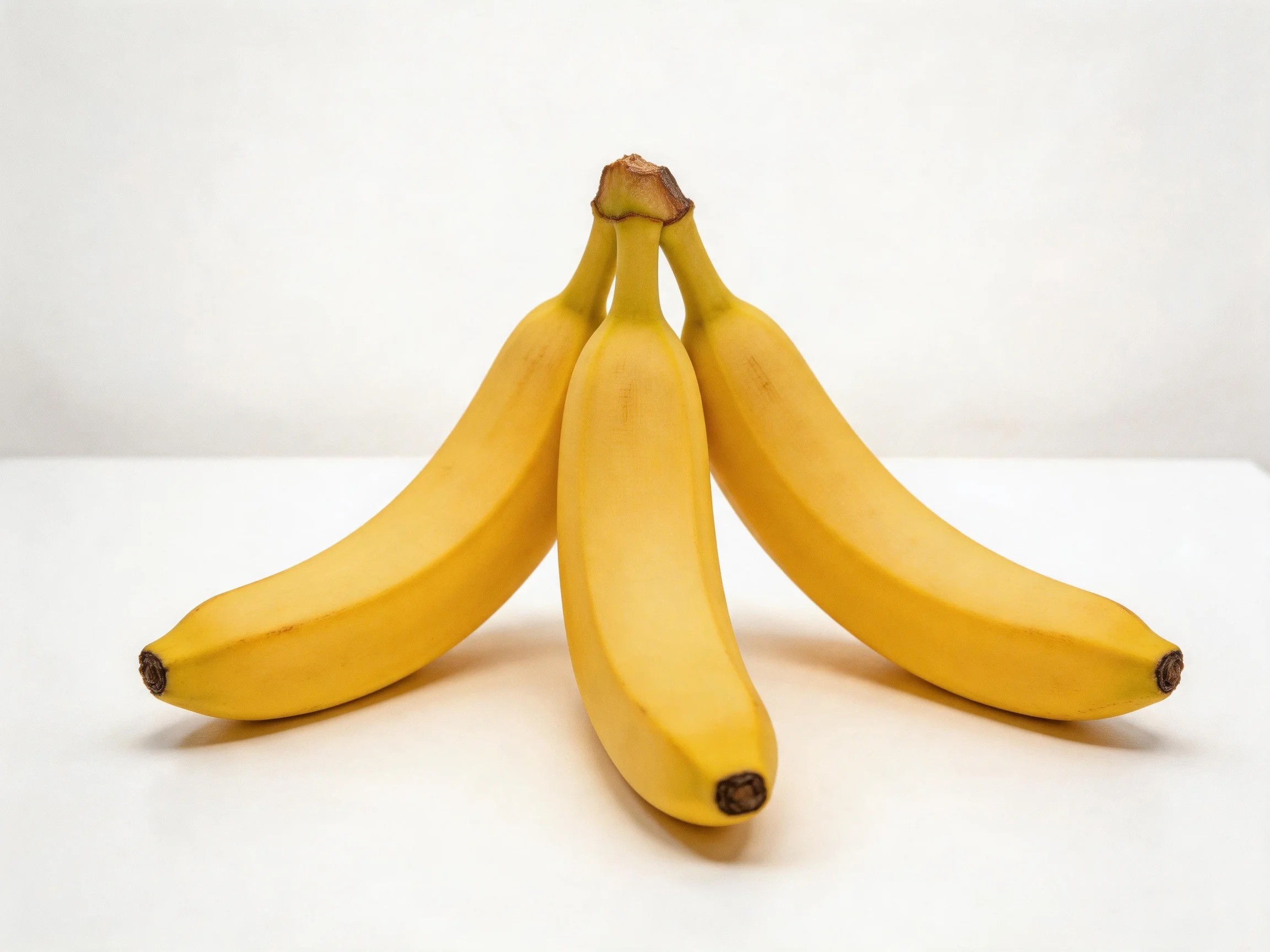 Three ripe yellow bananas clustered together on a white surface
