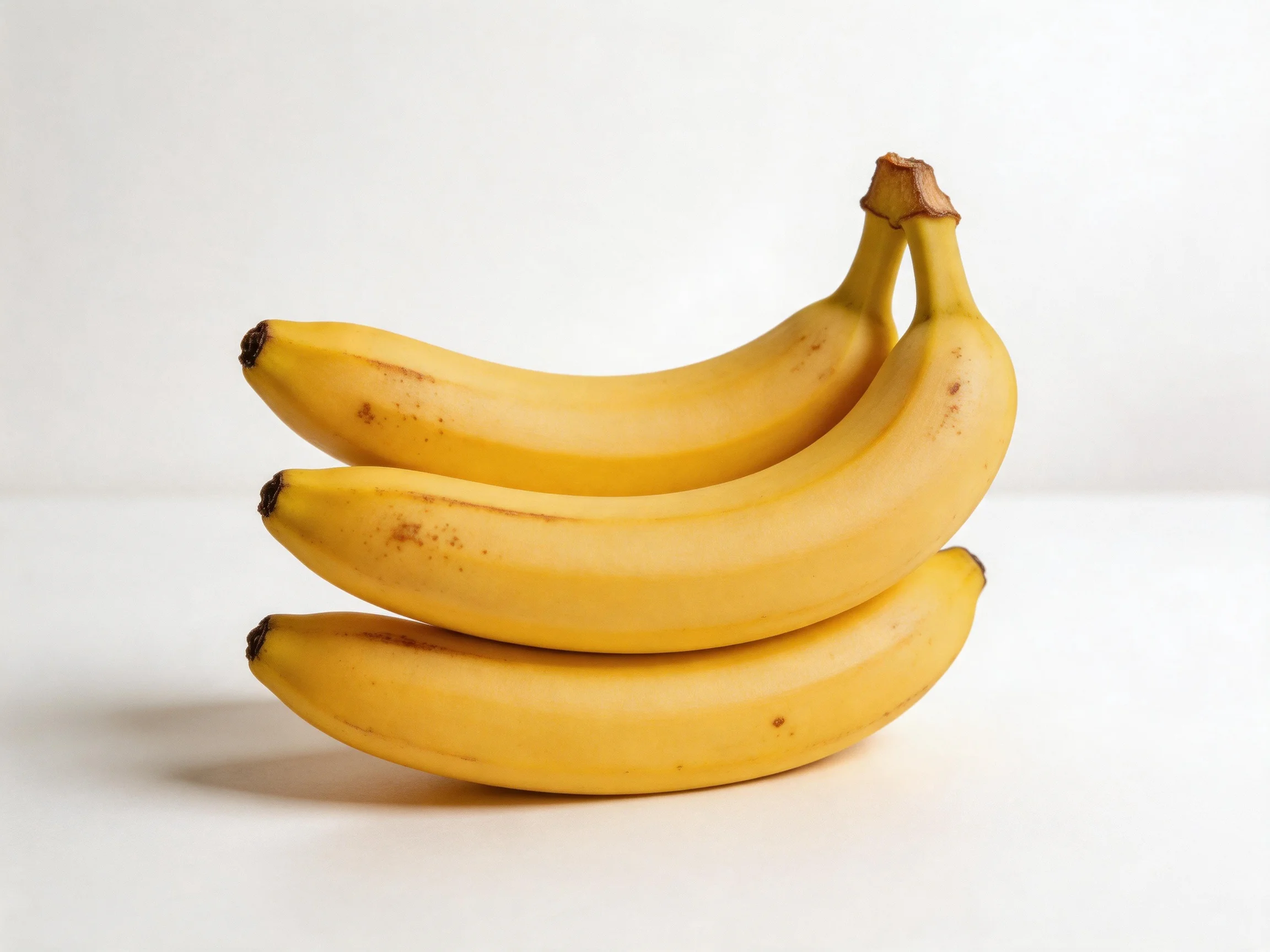 Three ripe yellow bananas stacked on a plain white surface