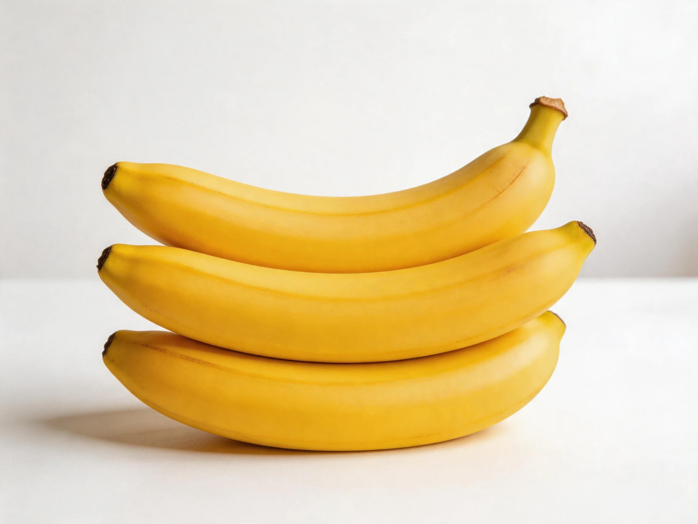 Three ripe yellow bananas stacked vertically on a white surface