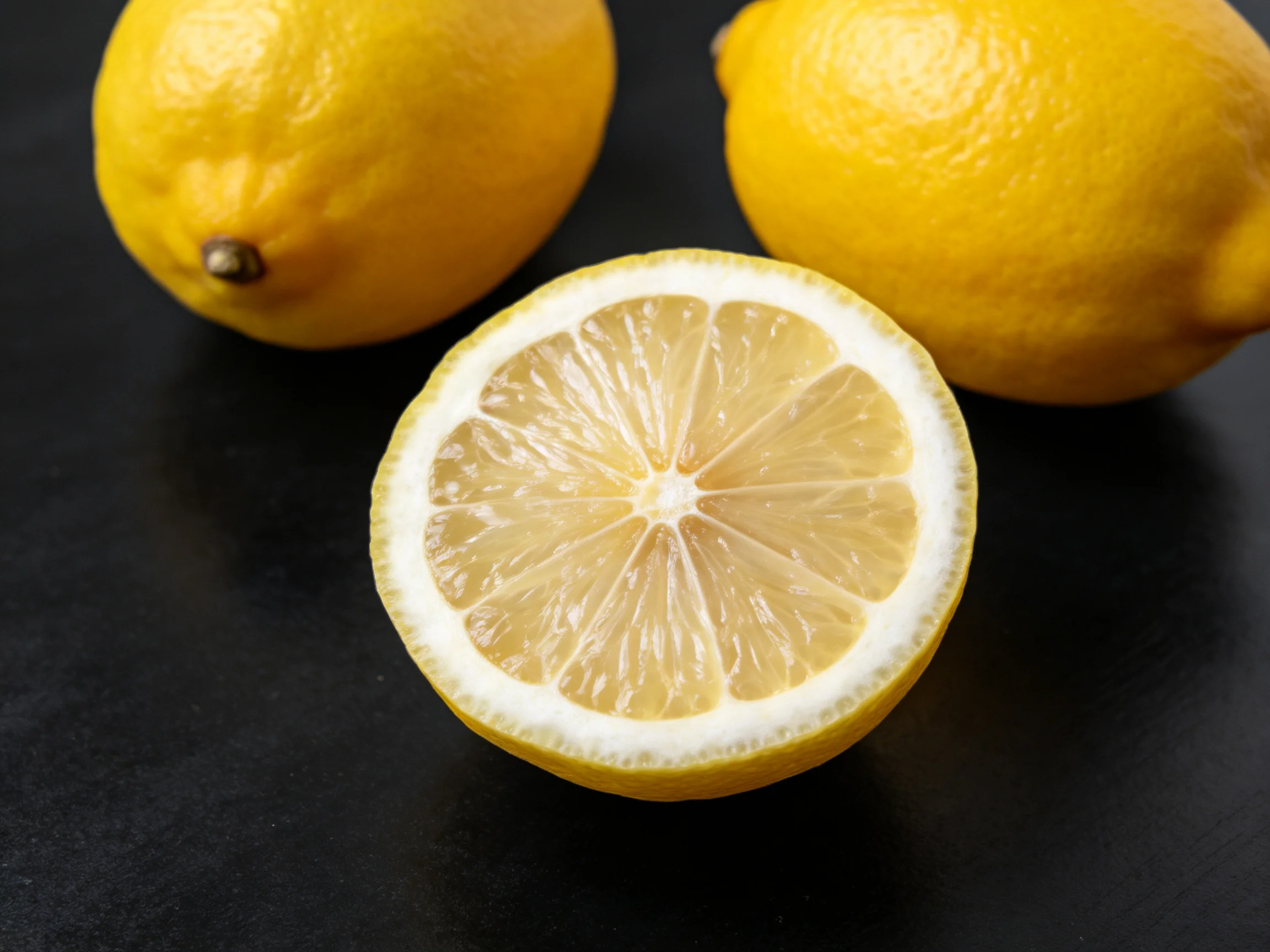 Three ripe yellow lemons, one sliced to display fresh interior