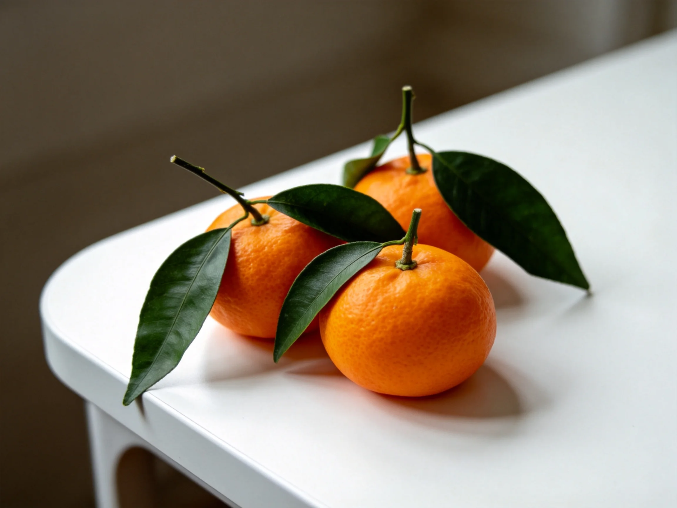 Three vibrant orange tangerines with dark green leaves on a white surface